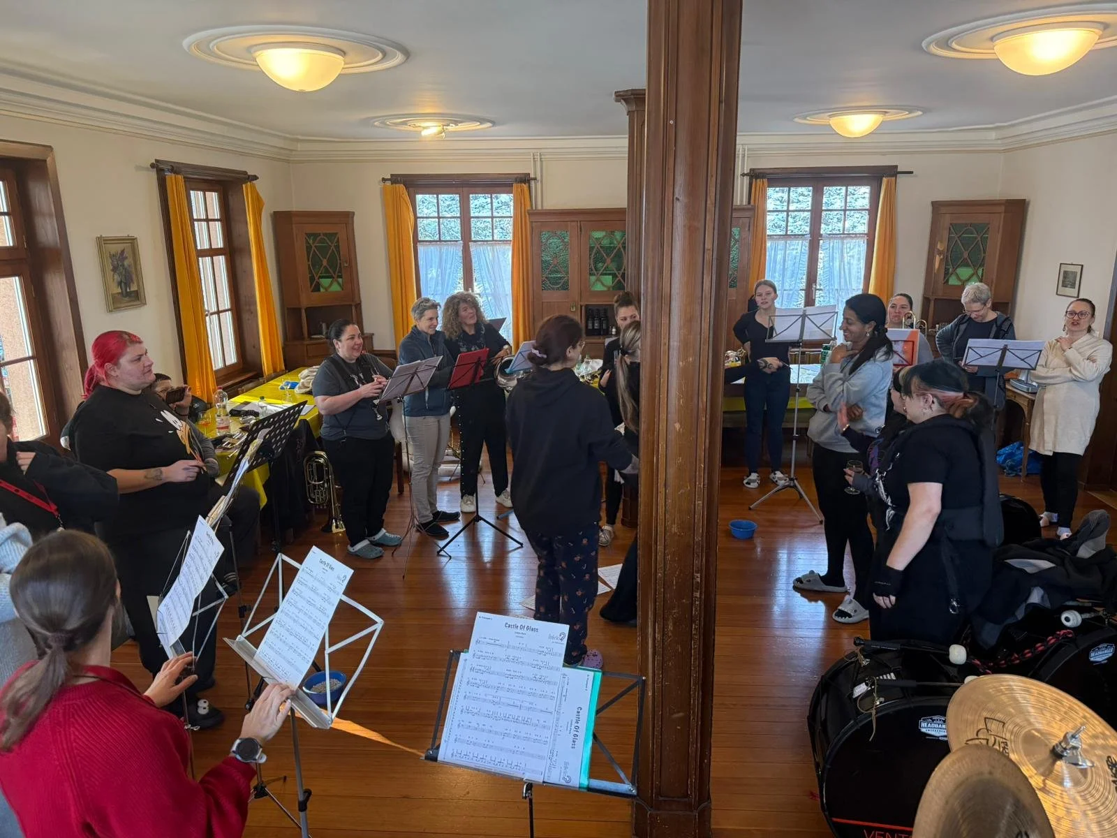 Eine Gruppe von Menschen in einem Musikraum mit Instrumenten und Notenblättern, die sich auf einen Proben- oder Unterrichtsabend vorbereitet.