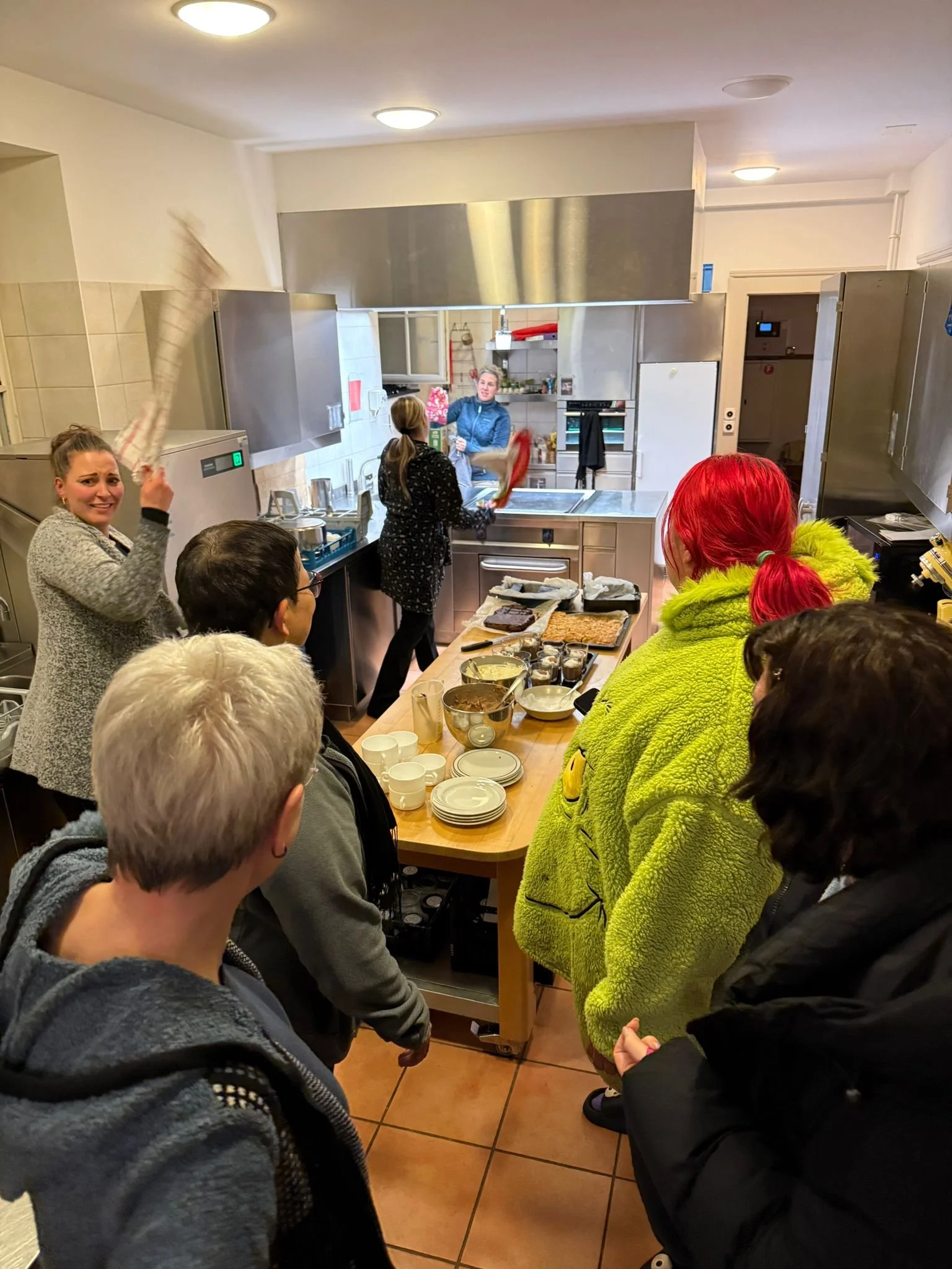 Mehrere Menschen in einer Küche, die an einem Kochkurs oder einer Kochvorführung teilnehmen.