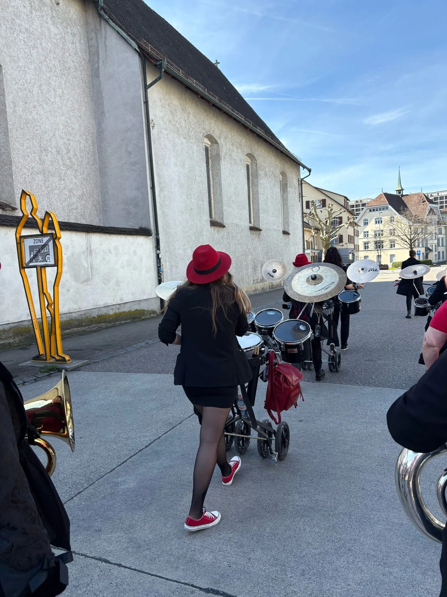 Menschen, die eine Blaskapelle auf einer Straße in der Stadt bei gutem Wetter spielen, mit einem Musiker, der einen Sousaphon trägt.