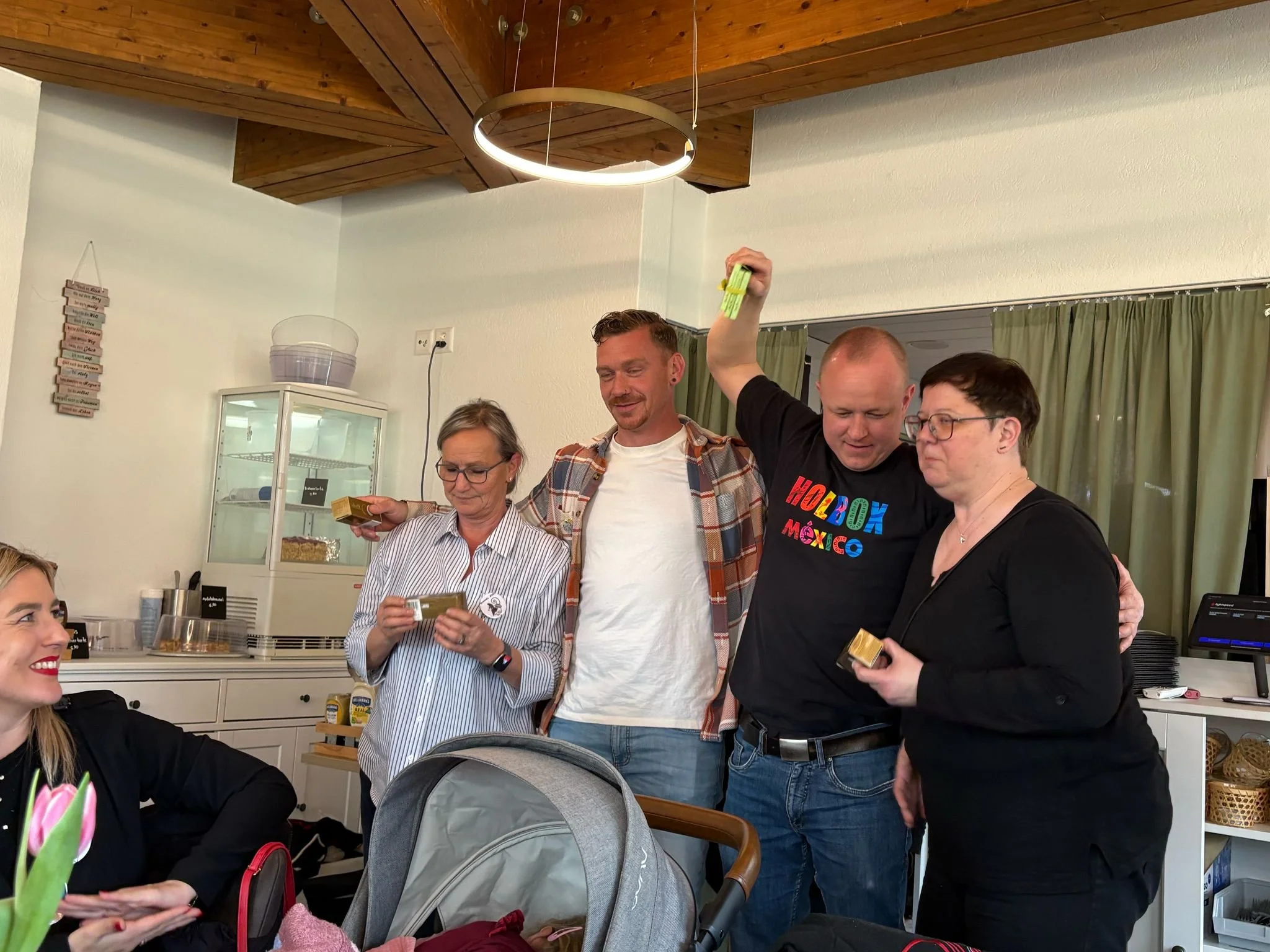 Menschen feiern gemeinsam in einem Raum, einige halten Geschenke und haben fröhliche Ausdrücke.