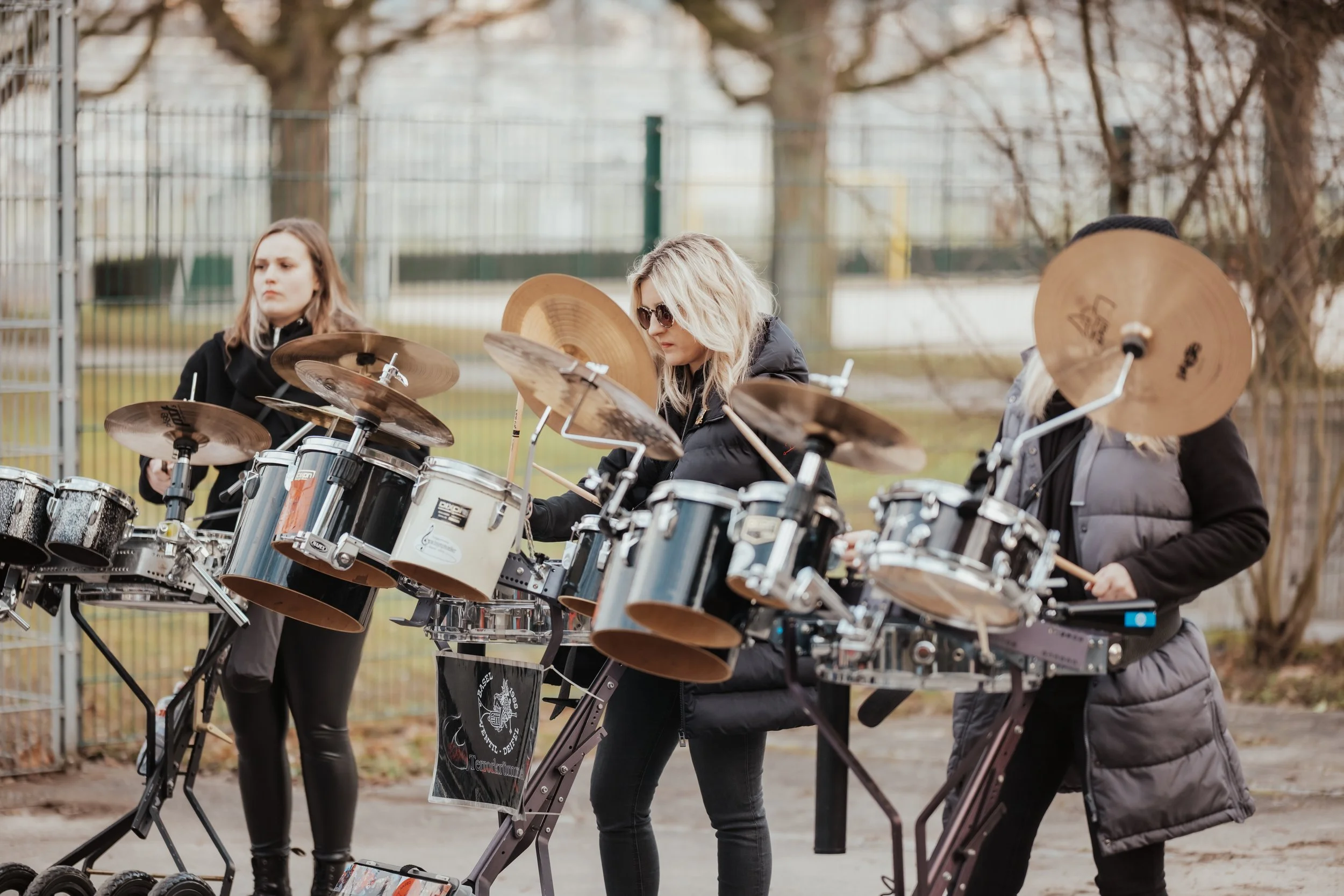 Drei junge Frauen spielen auf Perkussionsinstrumenten im Freien.