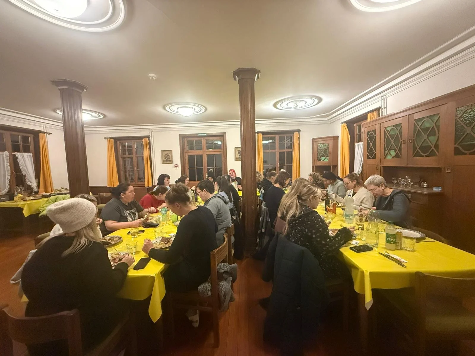 Menschen sitzen an Tischen in einem Restaurant, das mit gelben Tischtüchern bedeckt ist, beim Abendessen.
