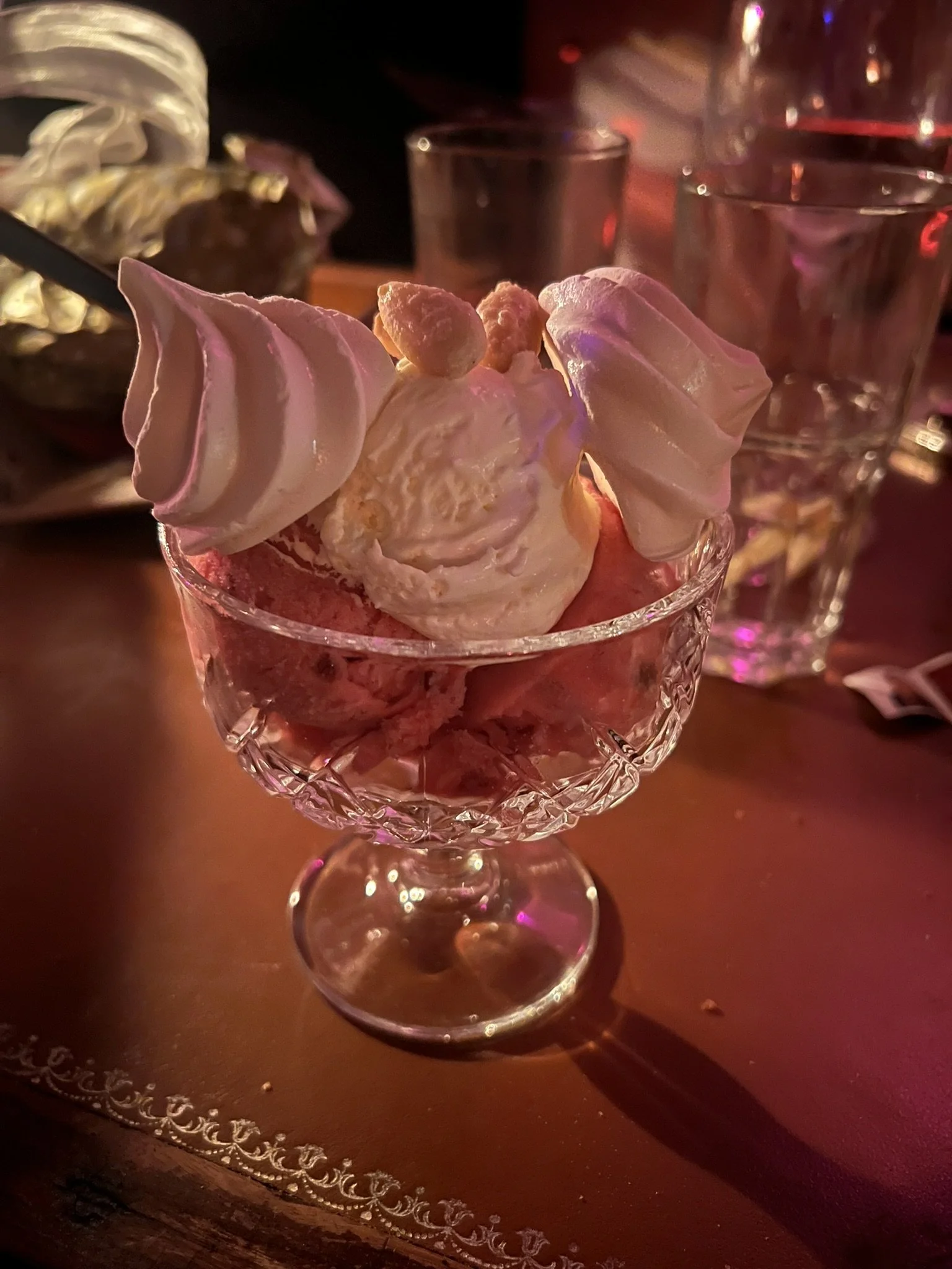 Ein Glasschälchen mit Eis und Sahne, garniert mit Baiser-Tupfen, auf einem roten Tisch in einer Bar oder einem Restaurant bei gedämpftem Licht.