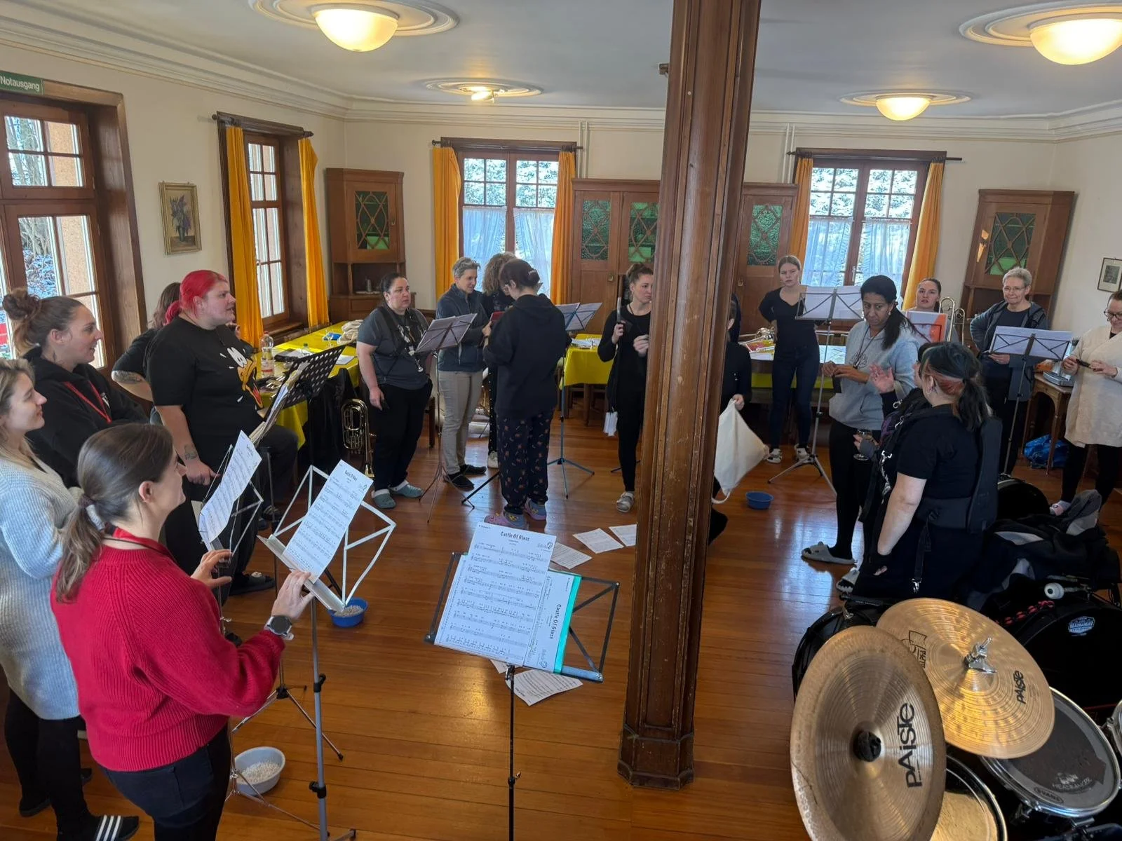 Chorprobe in einem gemütlichen Raum mit großen Fenstern, Holzfußboden und gelben Vorhängen.