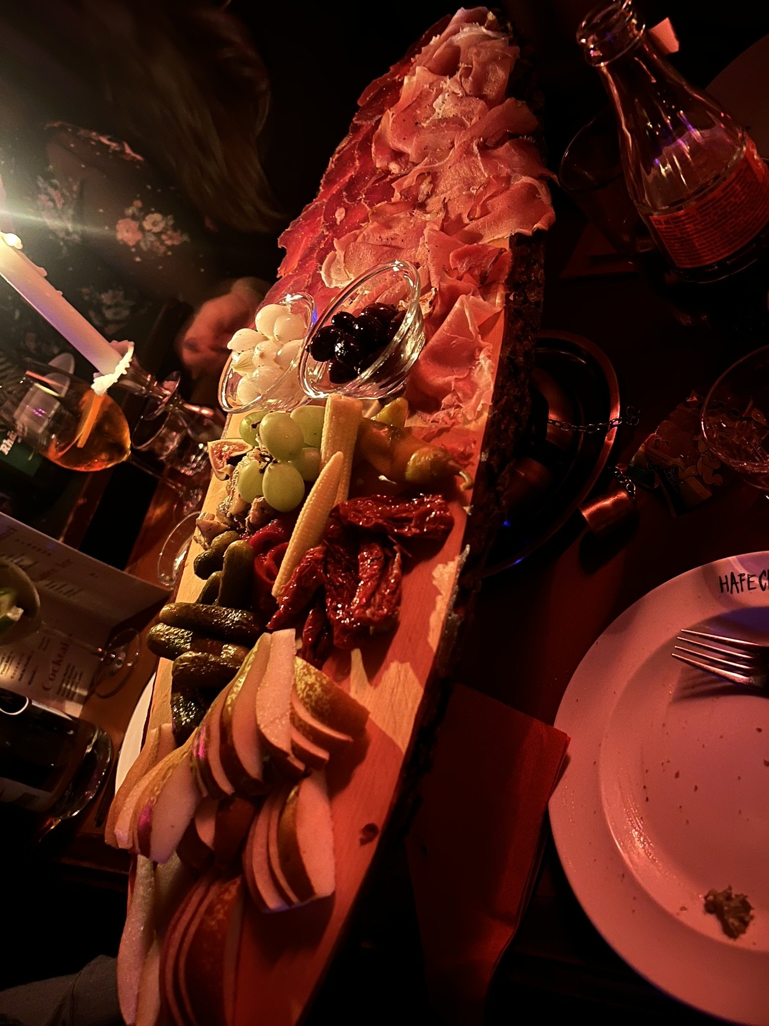 Brett mit verschiedenen Wurst- und Fleischsorten, Käse, Trauben, Oliven, eingelegtem Gemüse, getrockneten Tomaten, Johannisbeeren, Gurken und anderen Snacks, bei einem festlichen Anlass.