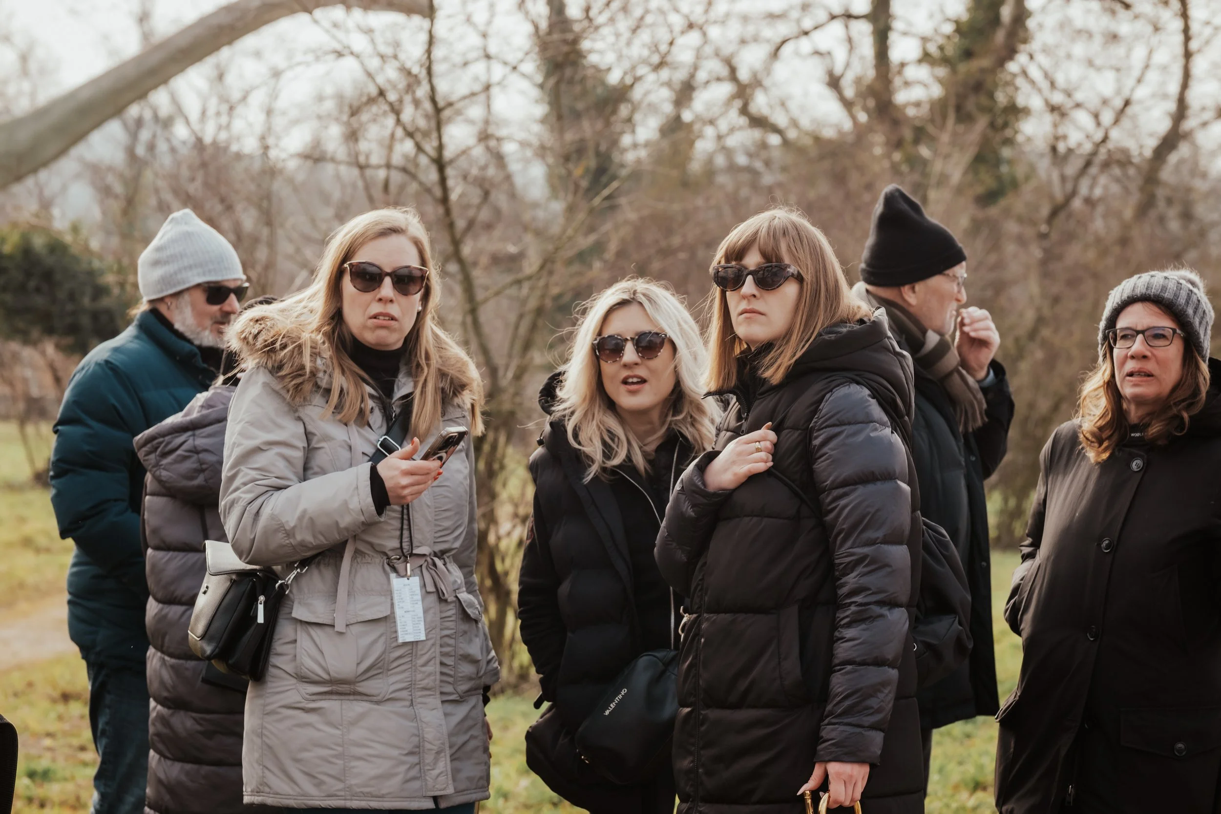 Gruppe von sechs Menschen, die im Freien stehen, tragen winterliche Kleidung und Sonnenbrillen, scheint eine Tour oder ein Ausflug zu machen.