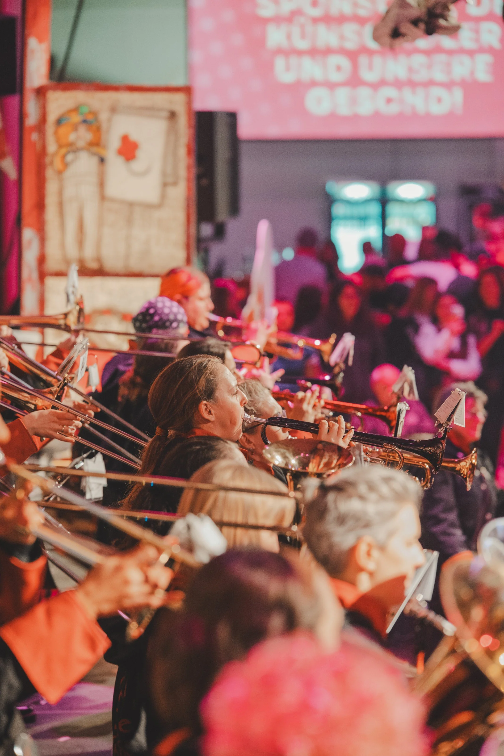 Orchester spielt bei einem Konzert, im Hintergrund eine rote Projektionswand mit weißen Texten.
