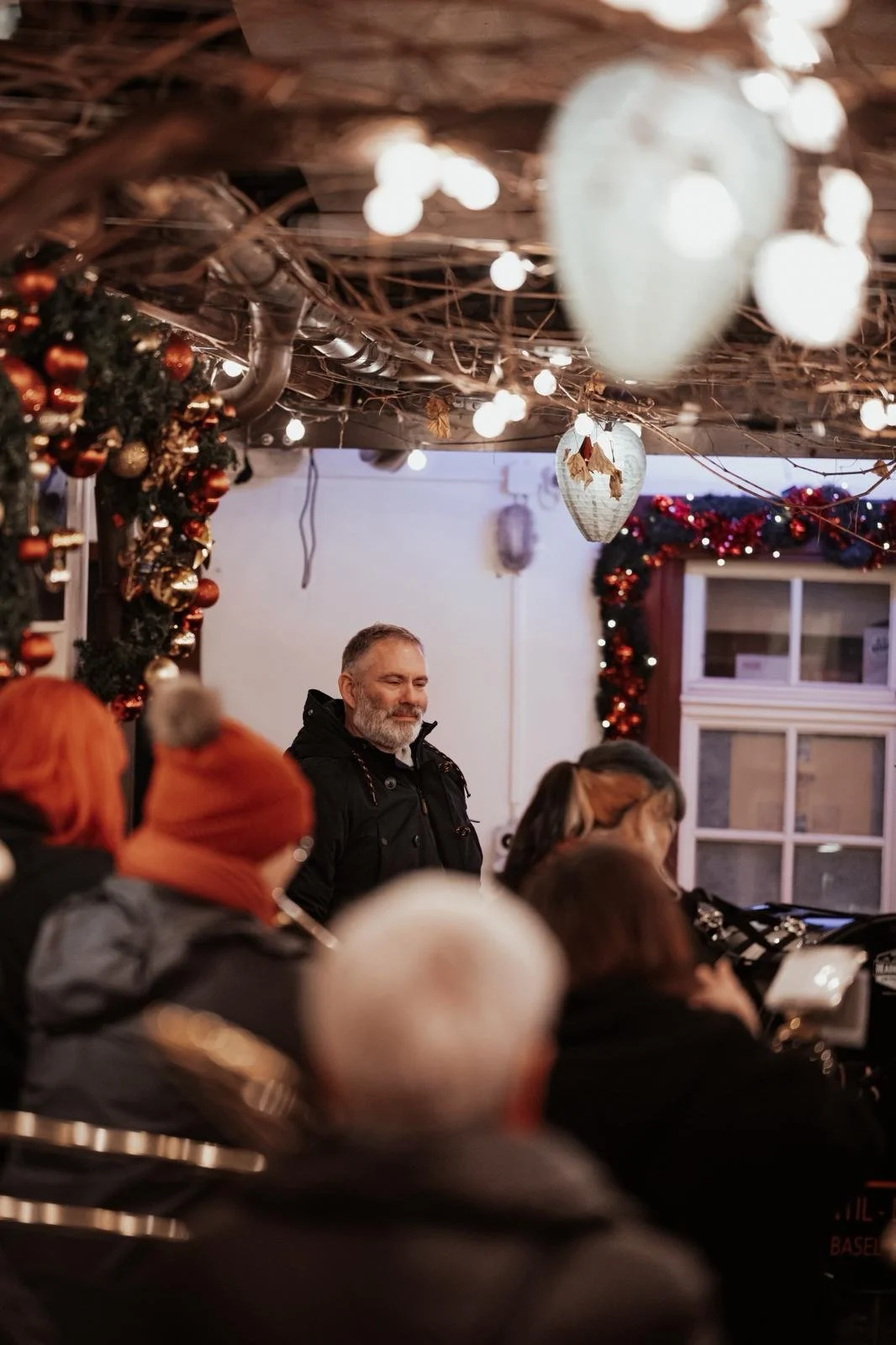 Eine Gruppe von Menschen in einem festlich dekorierten Raum, mit Weihnachtsgirlanden und Lichterketten, während eine Person im Mittelpunkt steht, wahrscheinlich bei einer Weihnachtsfeier oder Veranstaltung.