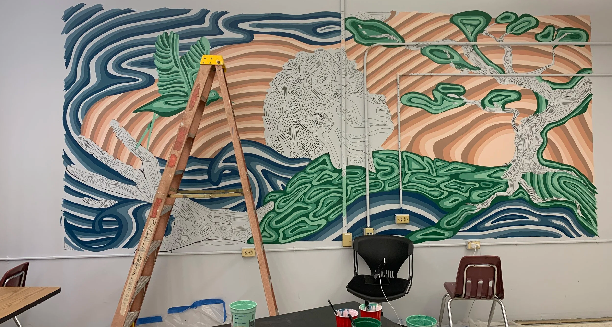 A mural in progress on a wall featuring a black and white outline of a face intertwined with abstract patterns, surrounded by colorful stylized foliage and flowing patterns, with painting supplies and a ladder in the room.