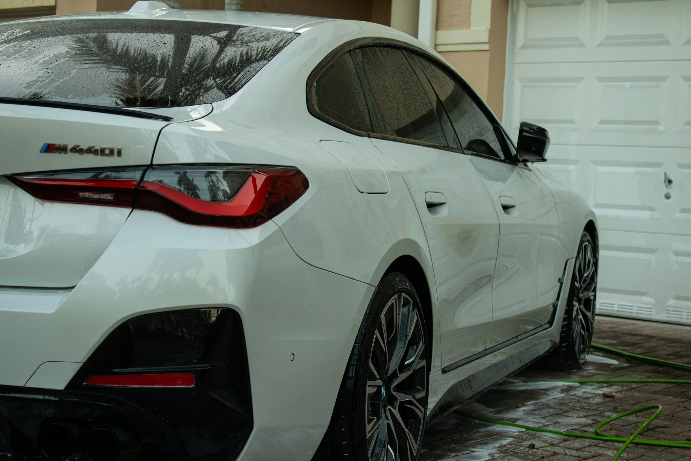White BMW M440i parked outside on wet pavement with a garage door in the background.