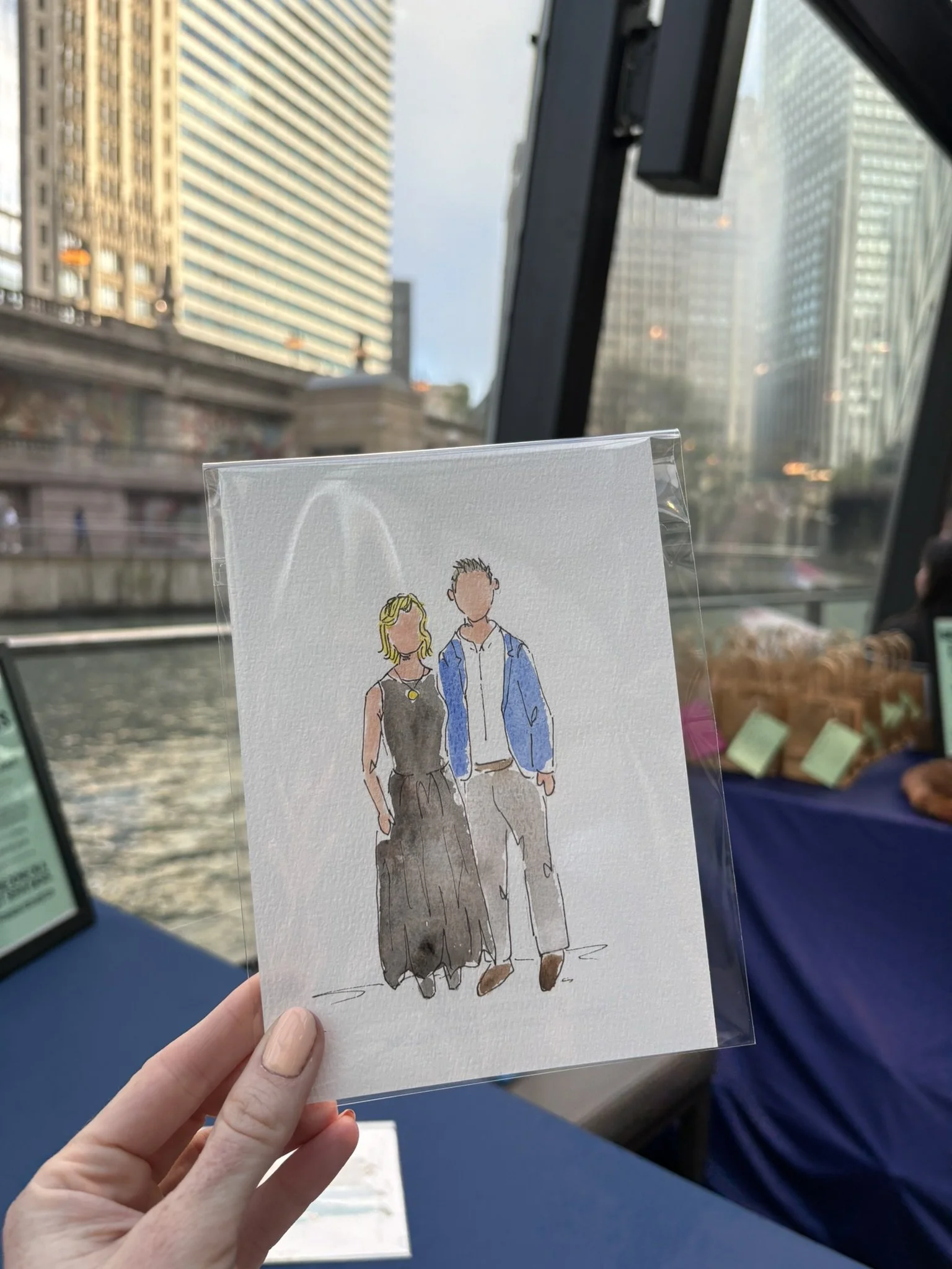 A person holding a watercolor illustration of a couple walking together, with a cityscape visible through a window in the background.