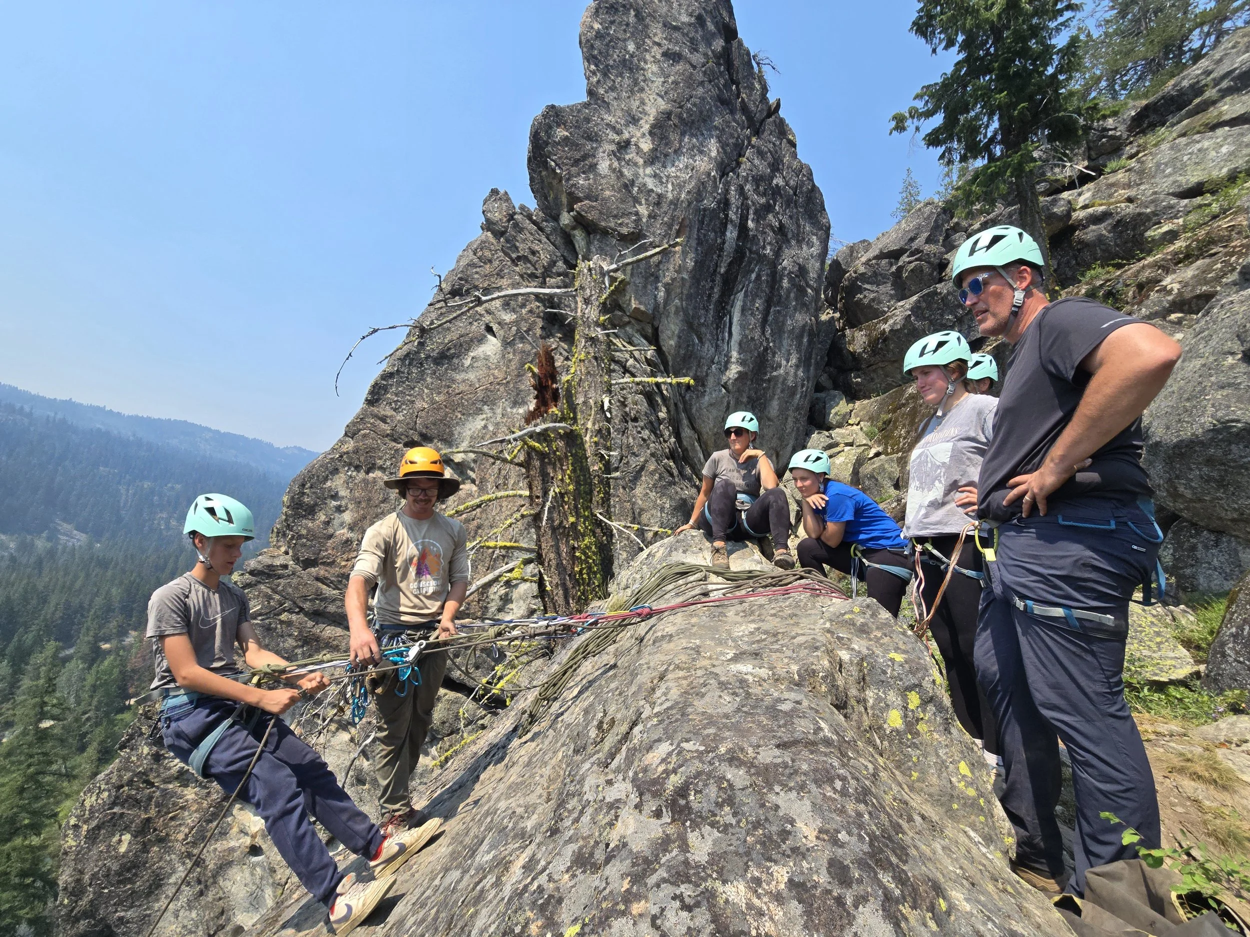 Collin demonstrates to a family how a rappel and back-up belay system work while a participant demonstrates.