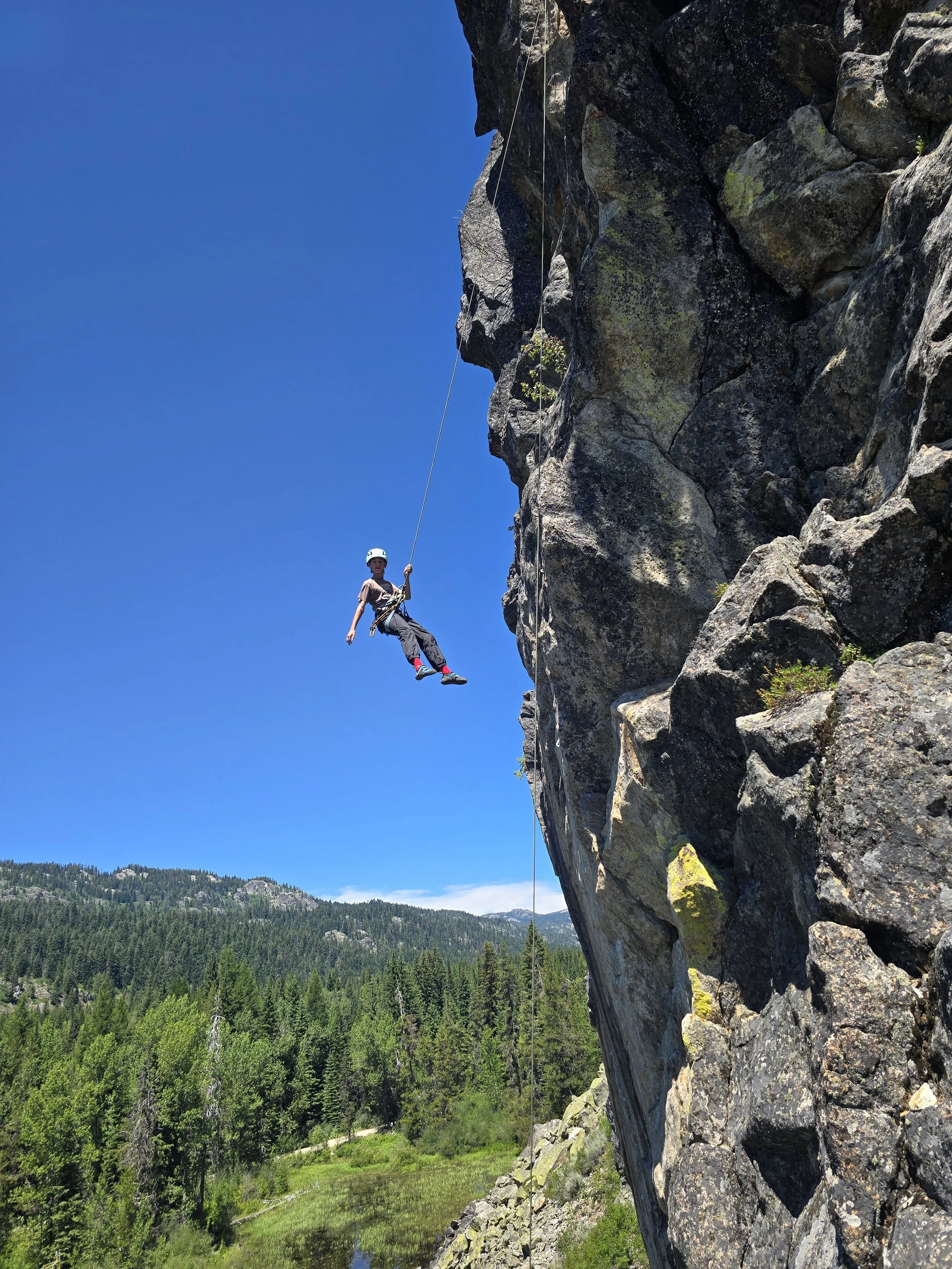 A young climber is seen floating in space as he gets comfortable putting his weight on the rope and swinging out.