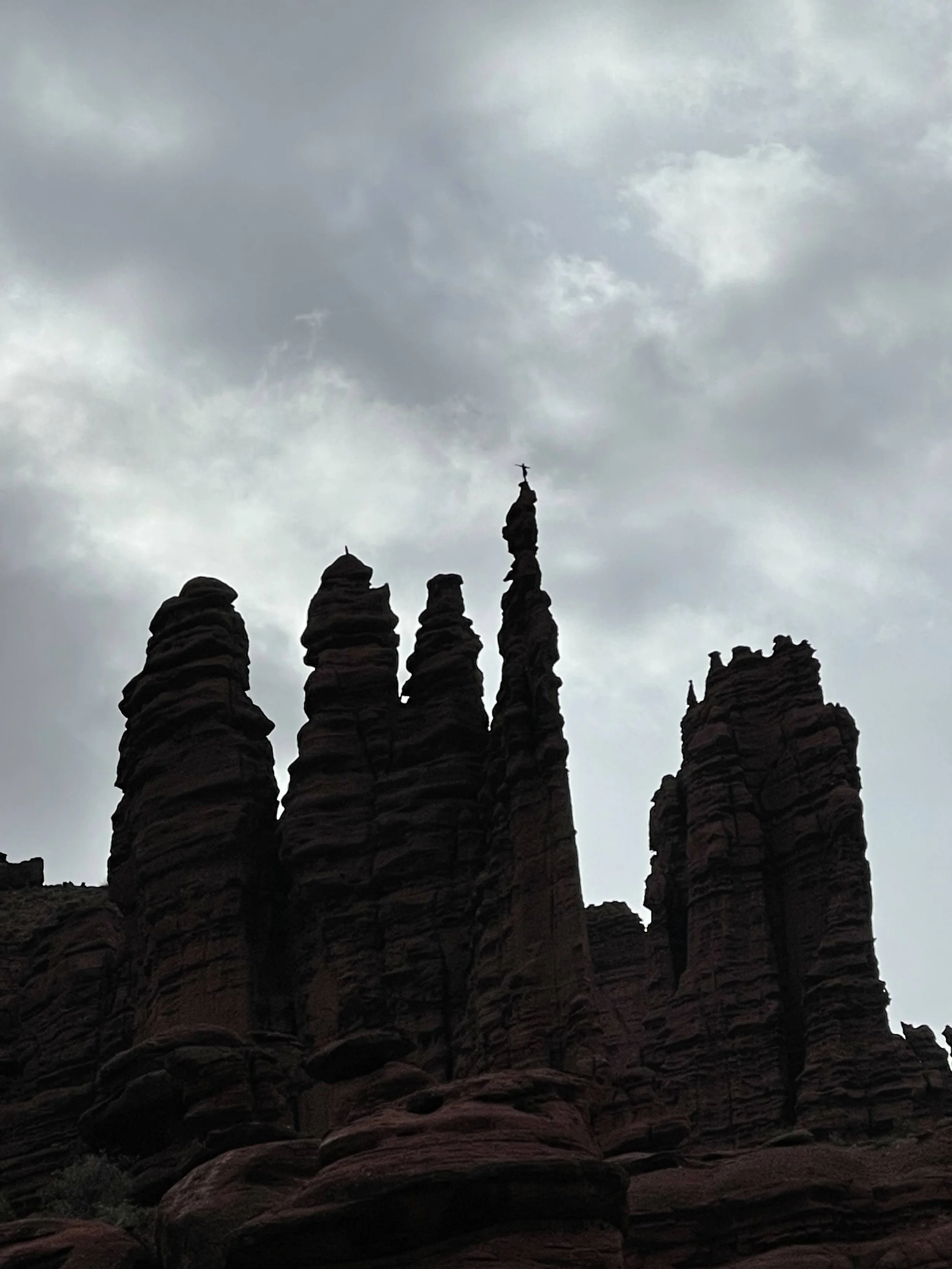 Silhouette of rock formations with cloudy sky in the background, including a tall formation with a cross at the top.