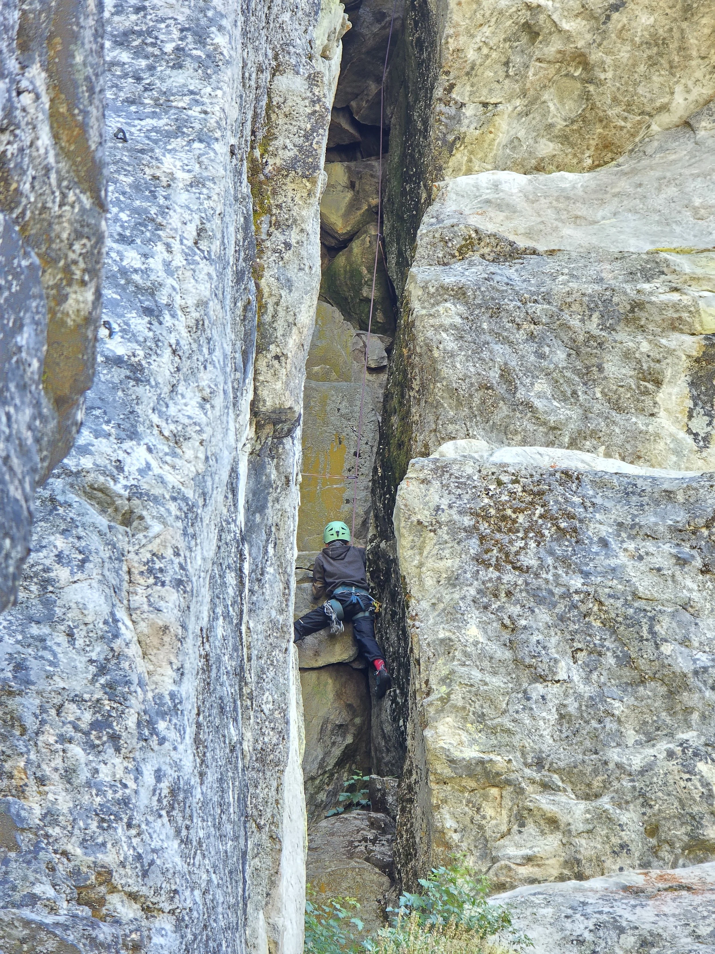 A young climber is climbing into the chimney on a trad route called "Unnamed Chimney"