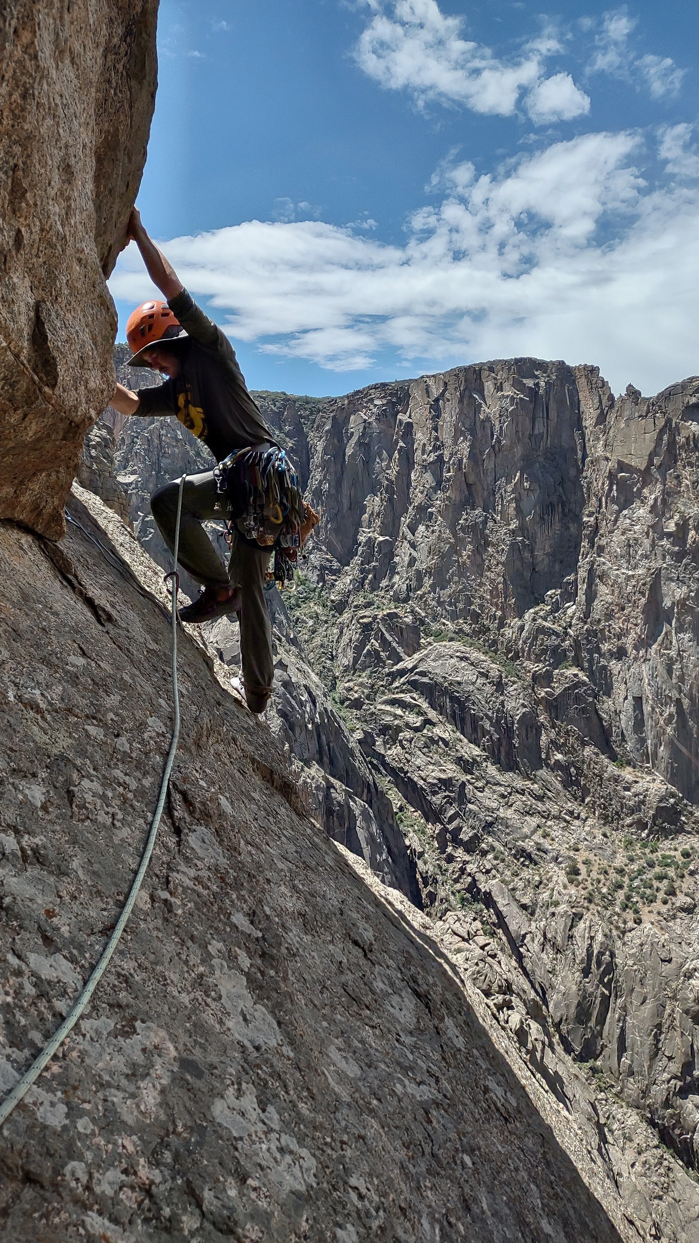 A climber wearing a helmet and harness ascending a steep rock face in a mountainous outdoor setting.
