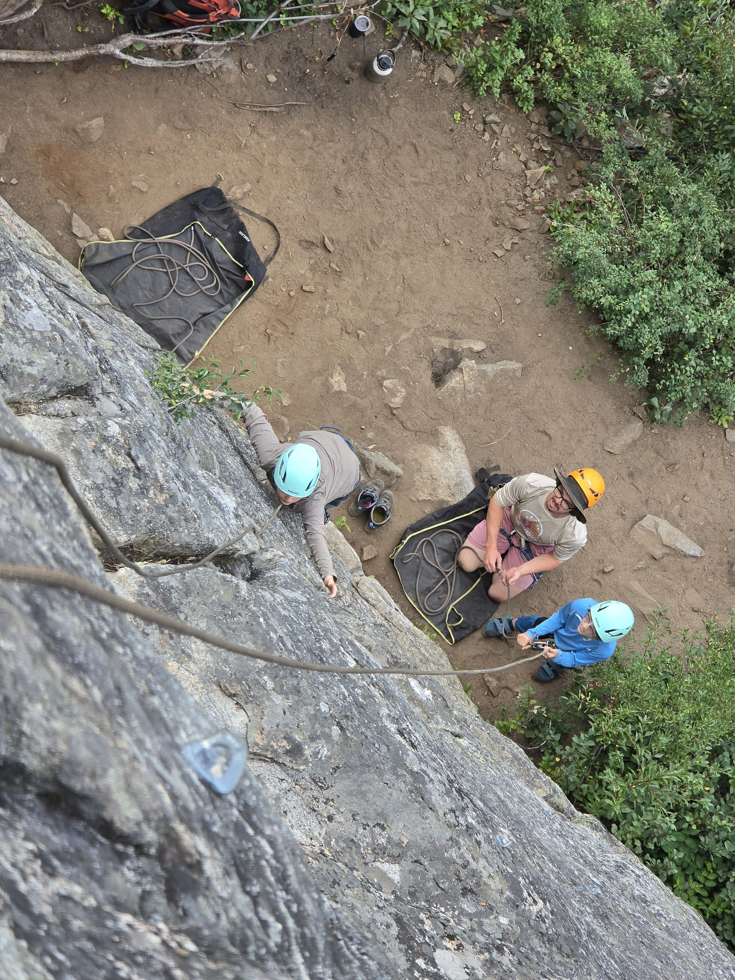 Collin is backing up a young climber as he learns how to belay while another participant climbs the wall.