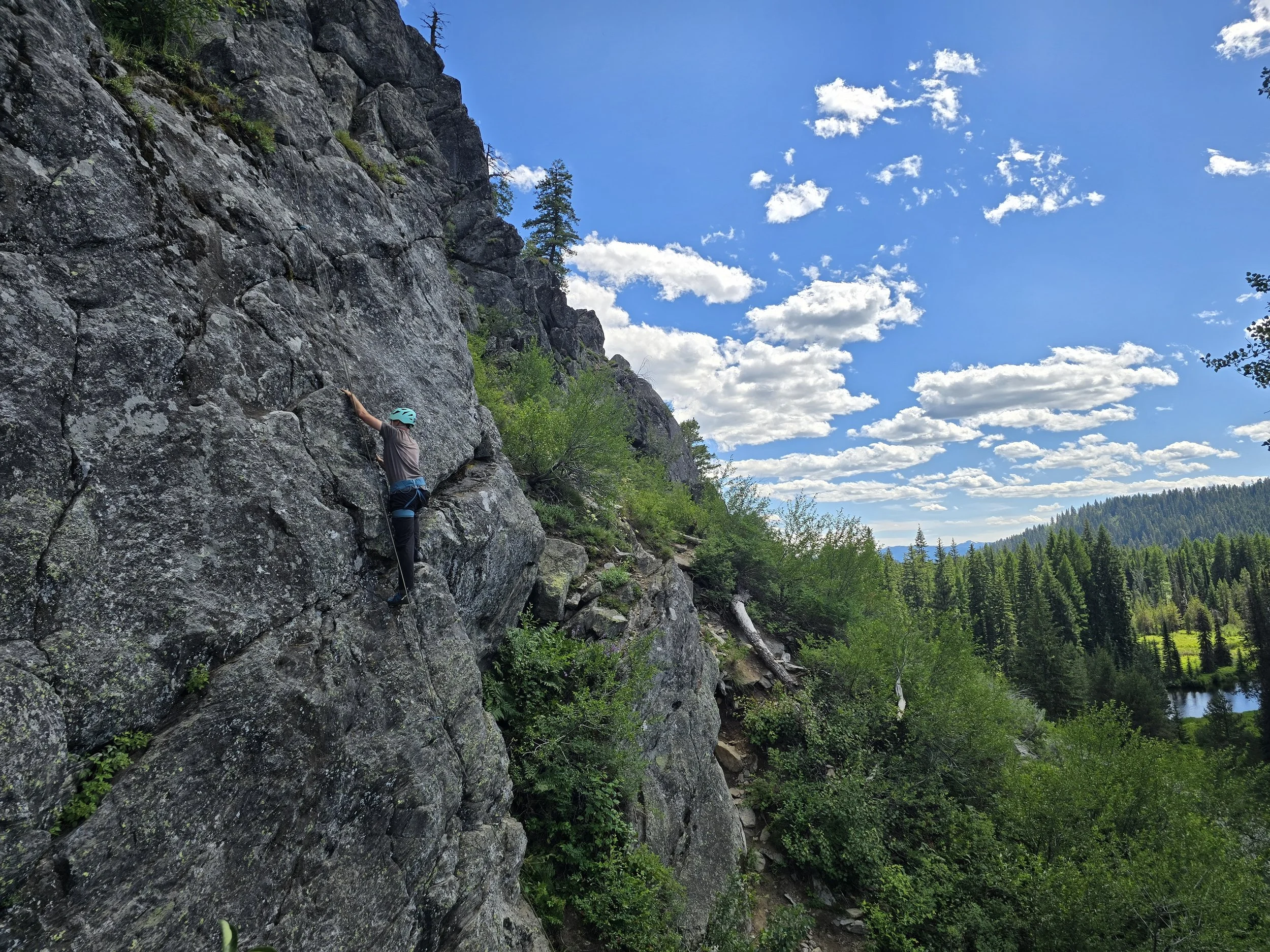 A climber is seen halfway up a climb with the Payette Lake seen in the distance.