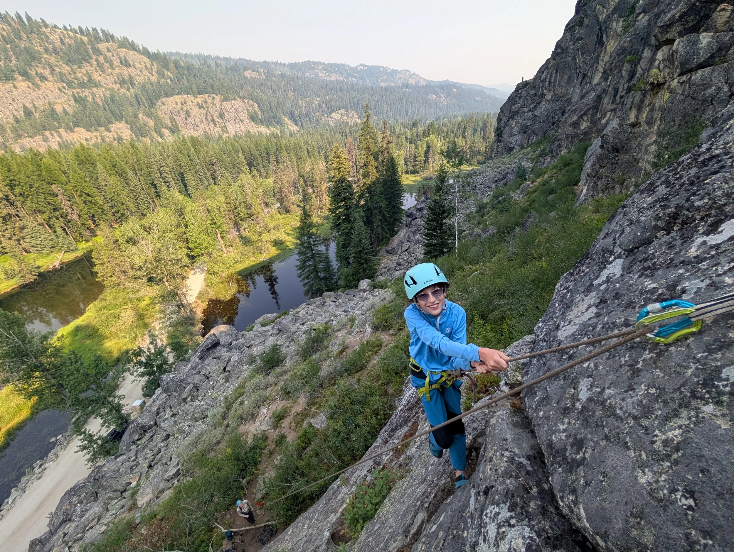 A young participant in our Four-week program smiles as he made it to the anchors at the top of a route with the Meanders north of Payette Lake below him.