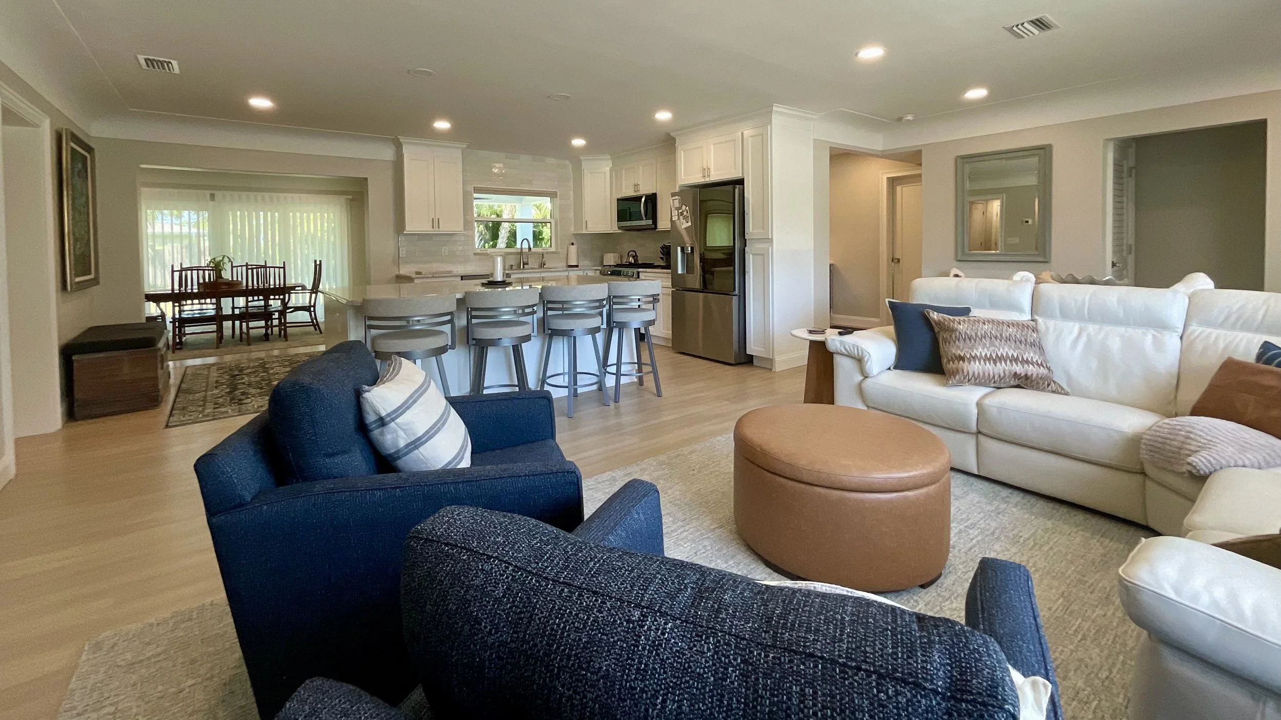 Open living, kitchen, and dining area with sliding glass doors overlooking future pool, featuring neutral and navy-toned decor and open sightlines.