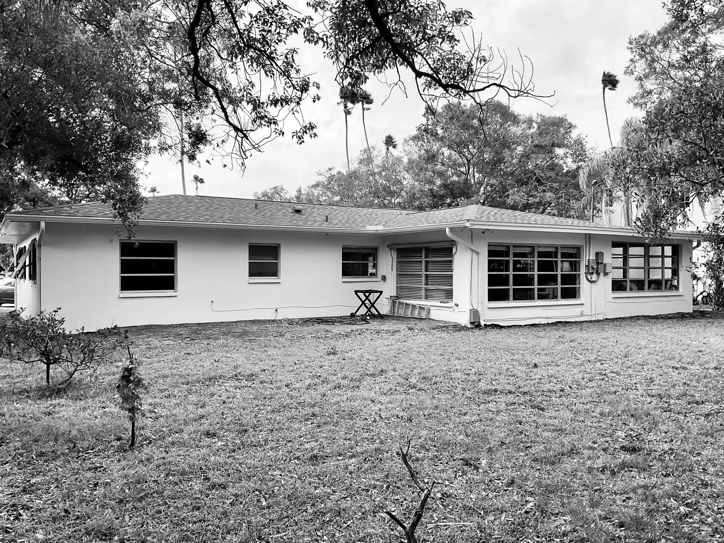 Black-and-white photo of home before remodel, showing rear elevation with large windows, no lanai, no bedroom addition, and no backyard access.