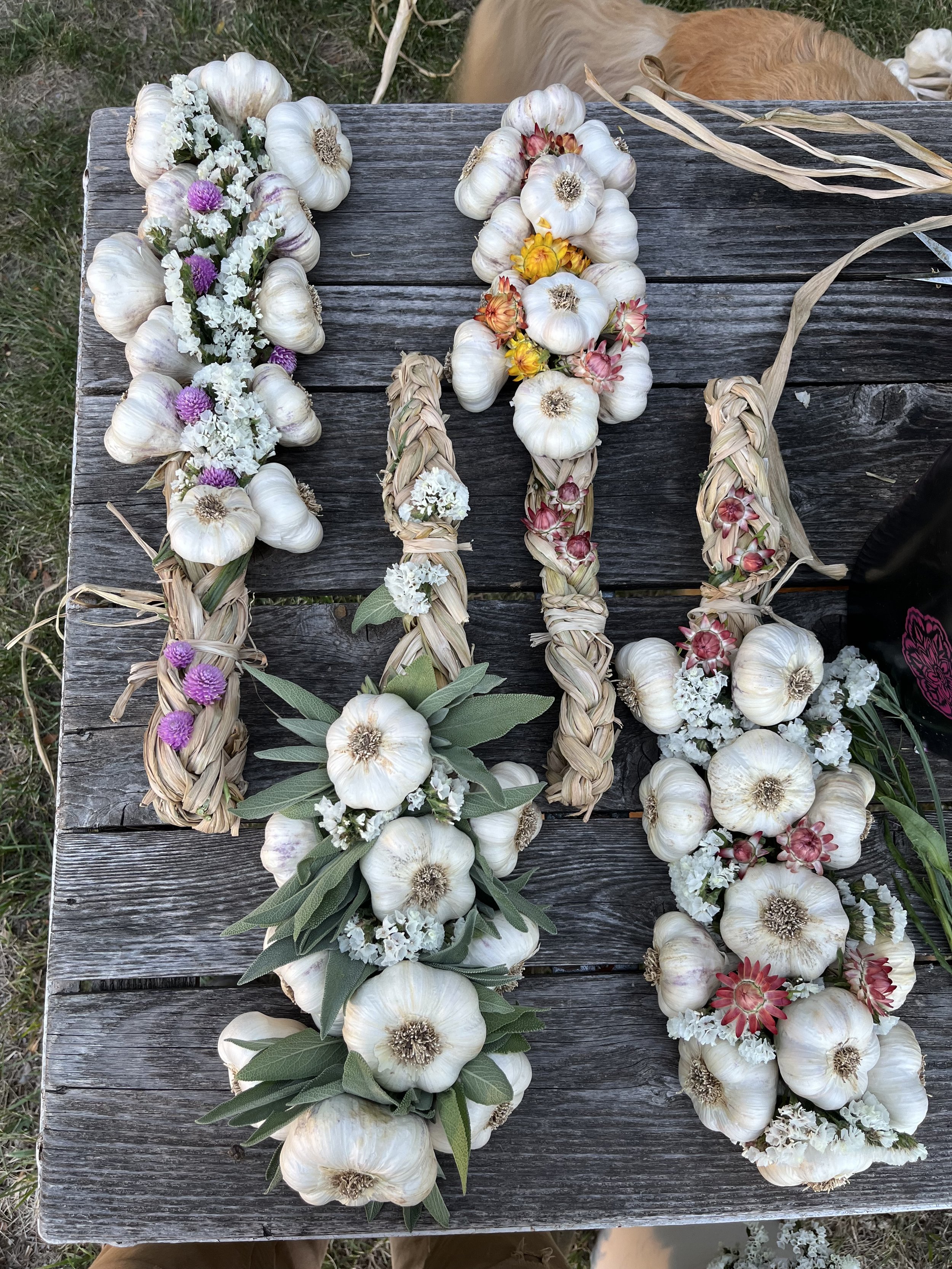 Garlic, artistically woven together like braids, with vibrant flowers laid on a rustic wooden surface.