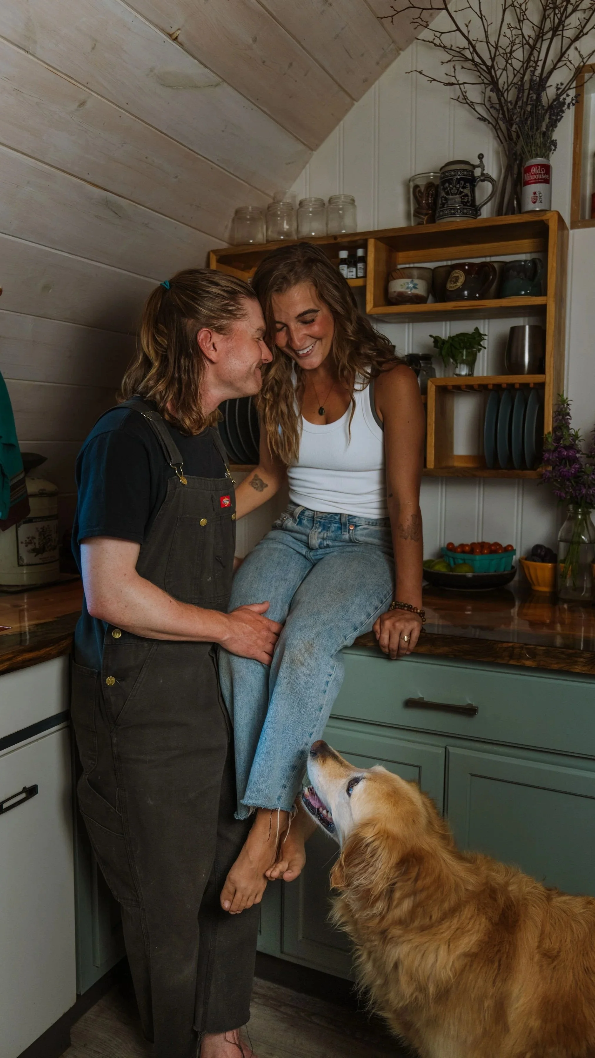A couple sharing a joyful moment in a cozy kitchen, with a loyal dog looking up at them.