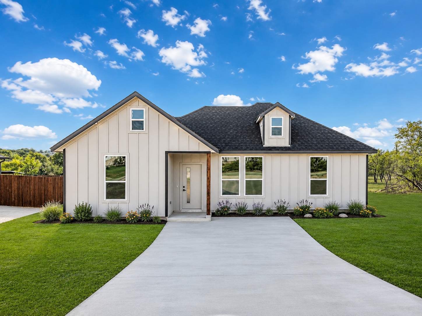 A new, modern house with a gray exterior and black roof, with a concrete driveway leading to the front door, under a blue sky with scattered clouds.