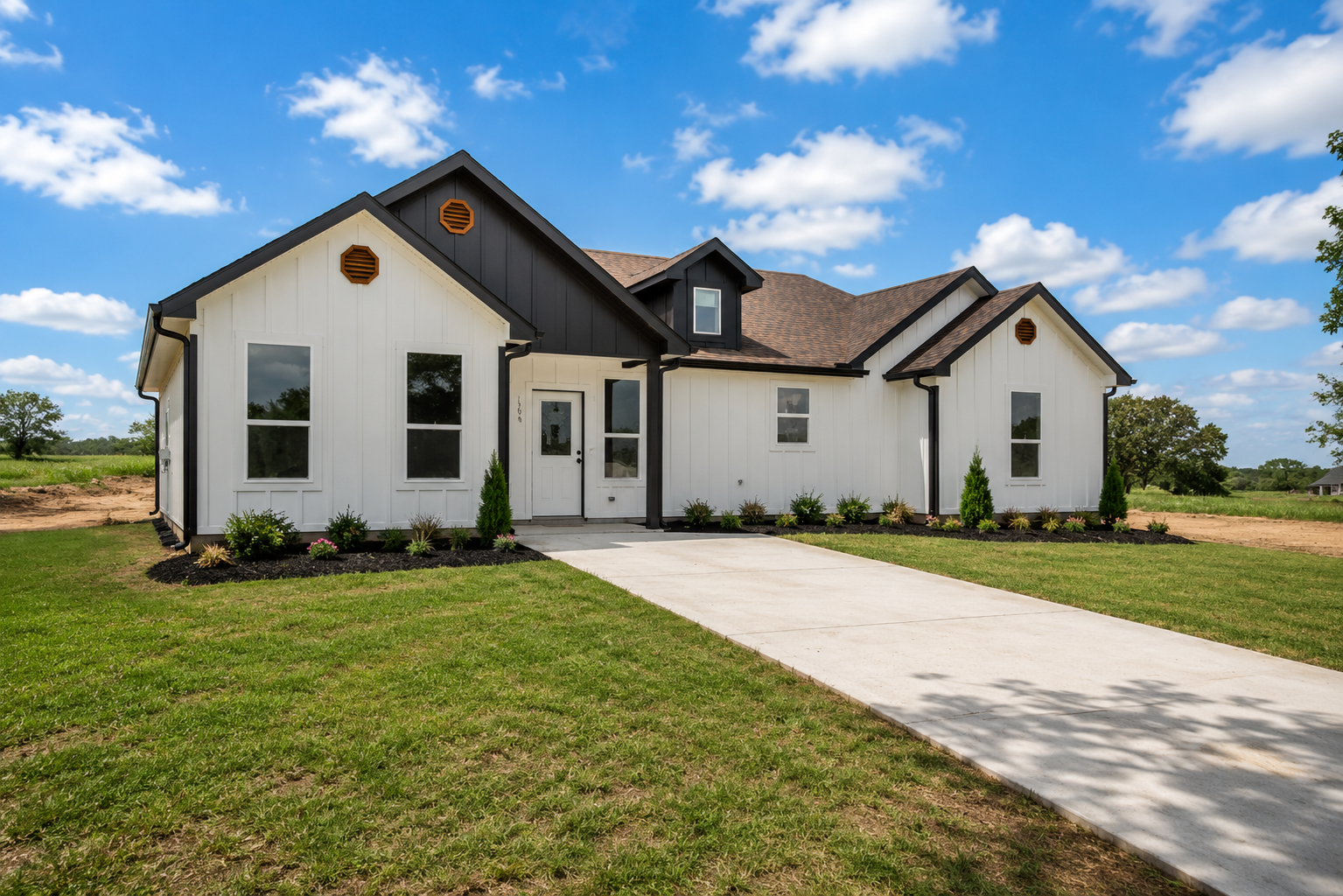 Newly constructed white house with black trim and a curved concrete driveway, under a partly cloudy sky.