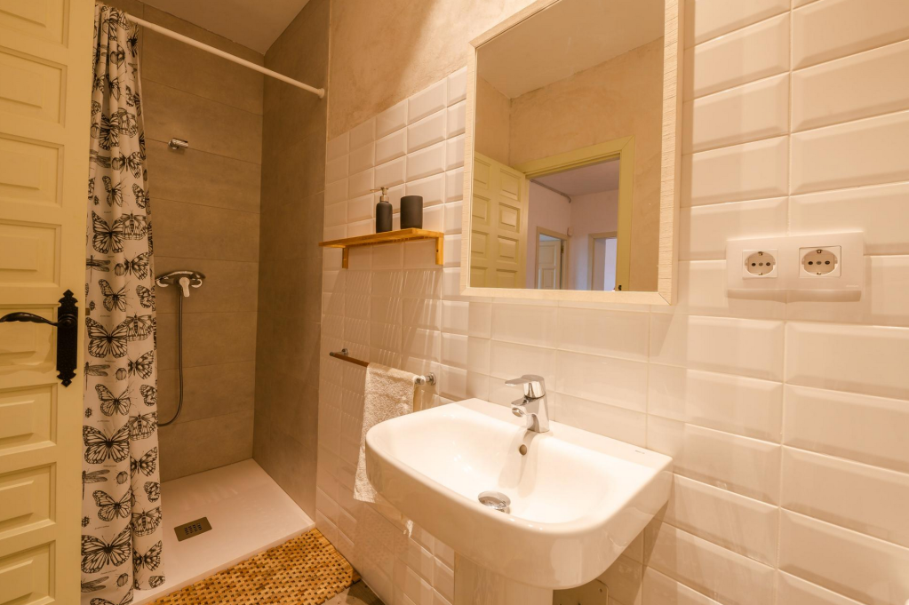 Bathroom with shower area, white sink, mirror, towel rack, butterfly patterned shower curtain, and power outlets.
