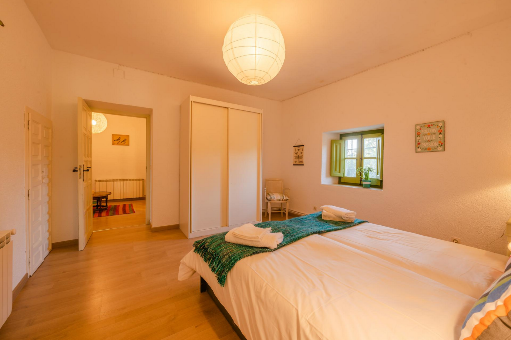 A cozy bedroom with a large bed, green accents, and a round paper lantern ceiling light.