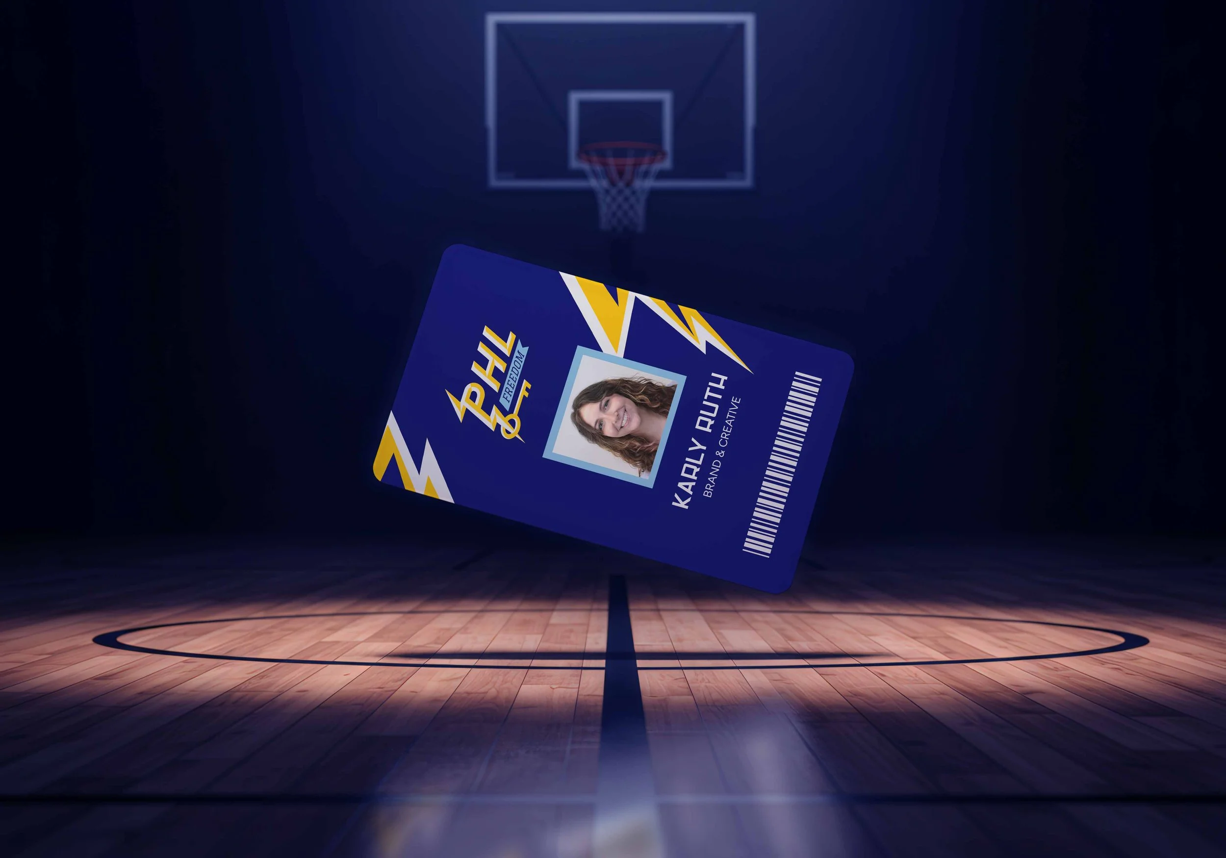 A single rectangular event credential badge with blue, yellow, and navy “PHL” lightning-inspired branding appears to float above a basketball court, lit with dramatic, cinematic arena lighting in the background.