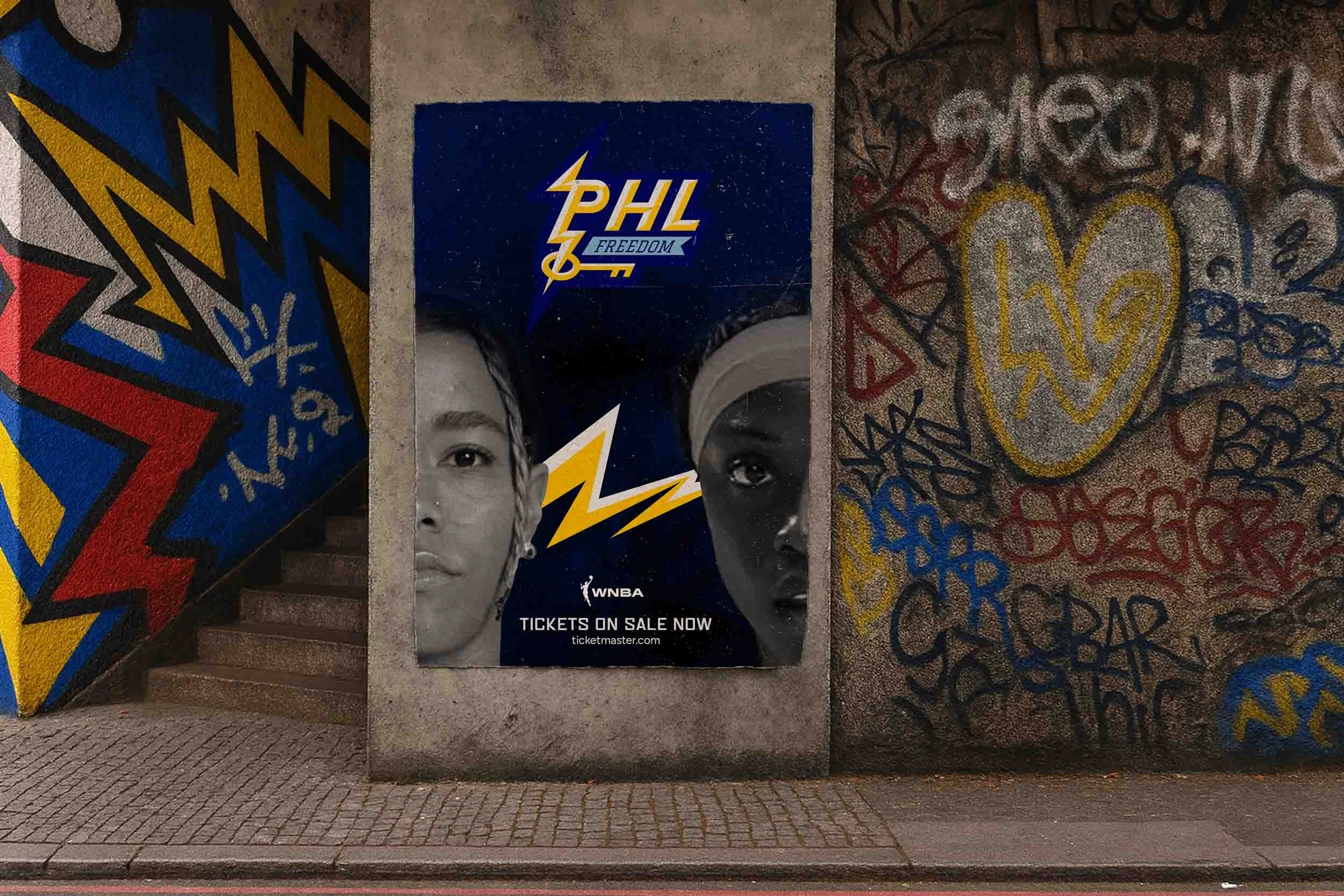 WNBA “PHL Freedom” poster with two players’ faces split by a yellow lightning bolt, displayed on a graffiti-covered wall.