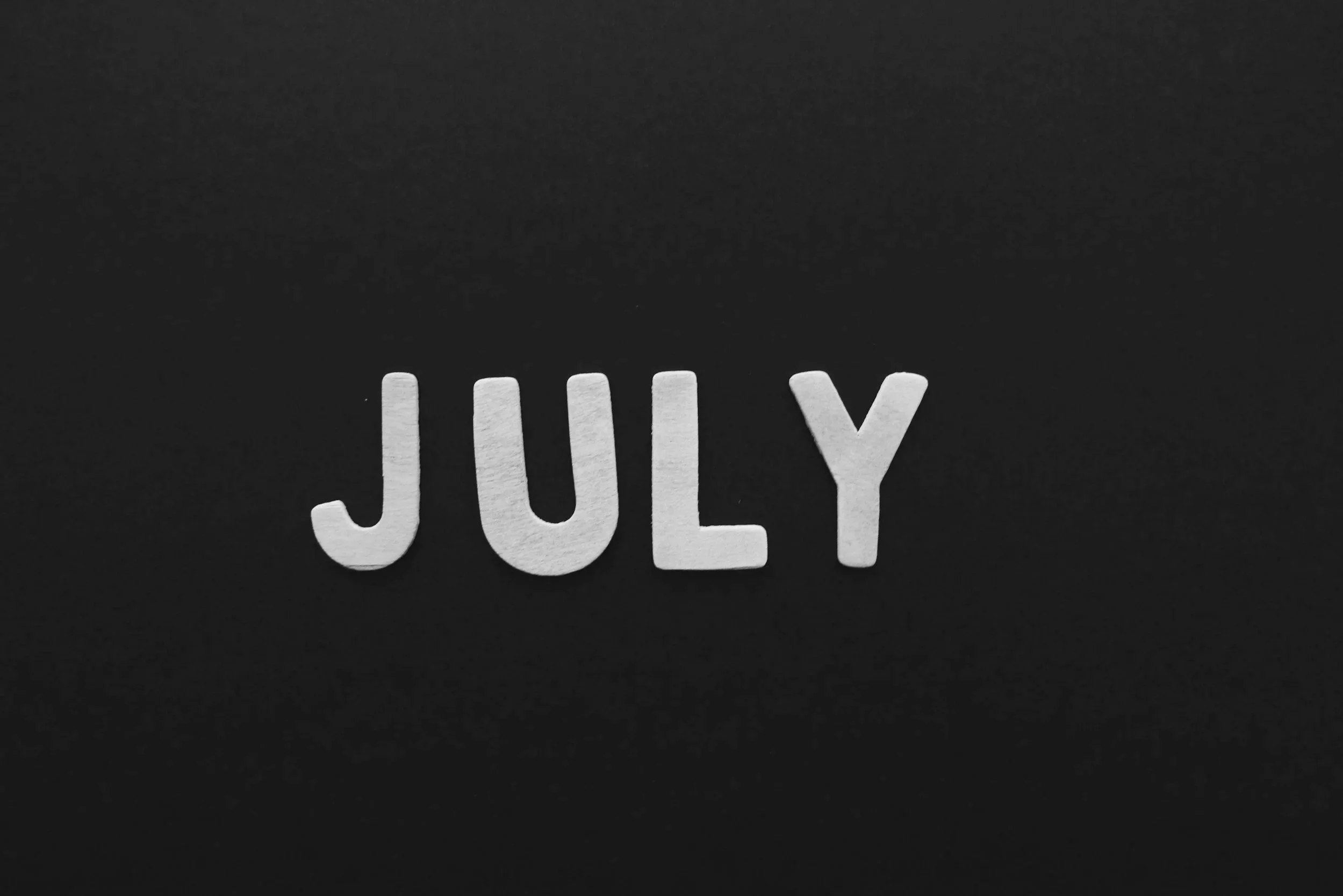 Black background with white wooden letters spelling 'JULY'.