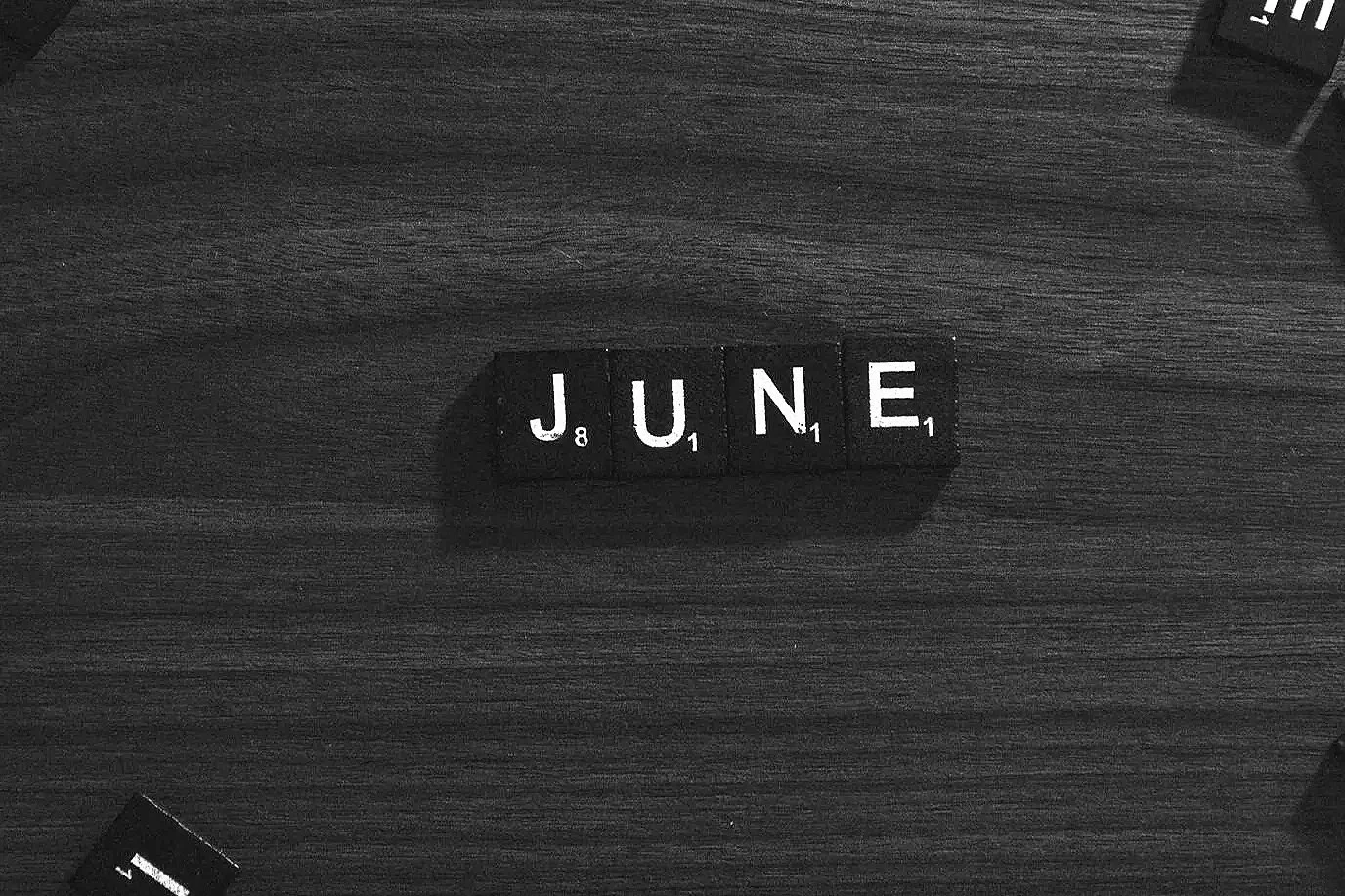 Black block tiles spelling 'JUNE' on a wooden surface.