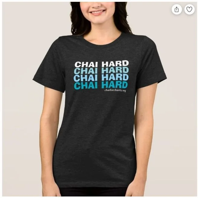 A woman wearing a black T-shirt with the repeated words 'CHAI HARD' in white and blue text, promoting chai tea charity.