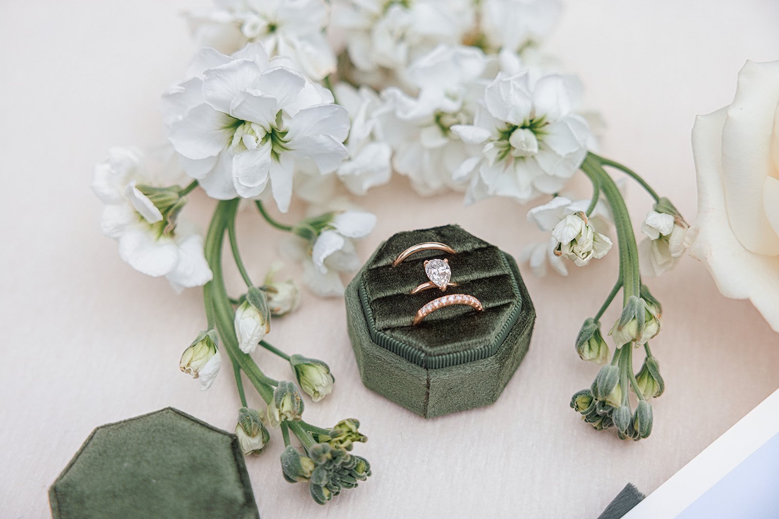 Three rings in a green velvet ring box surrounded by white flowers and green buds on a light background.