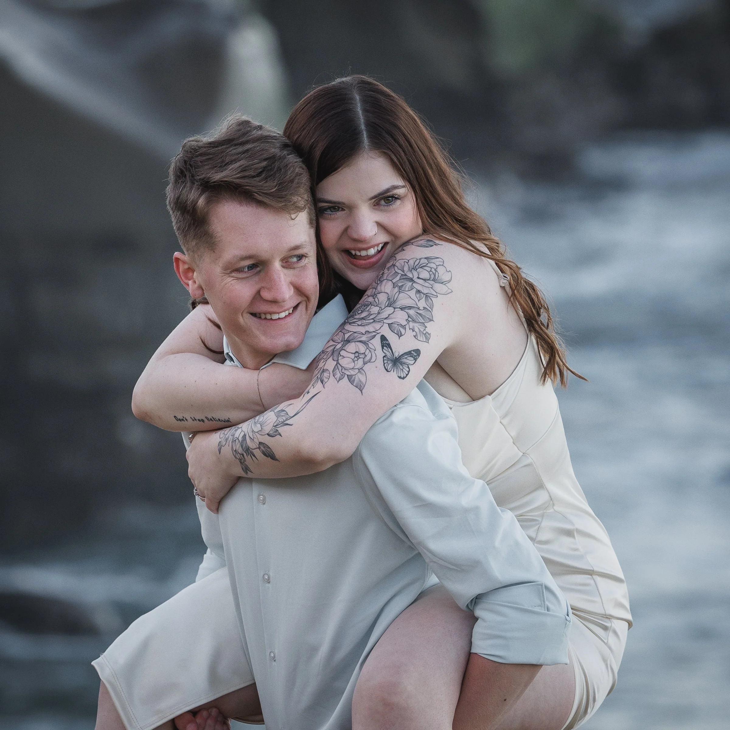 A couple at the beach, smiling and hugging each other, with the ocean in the background.