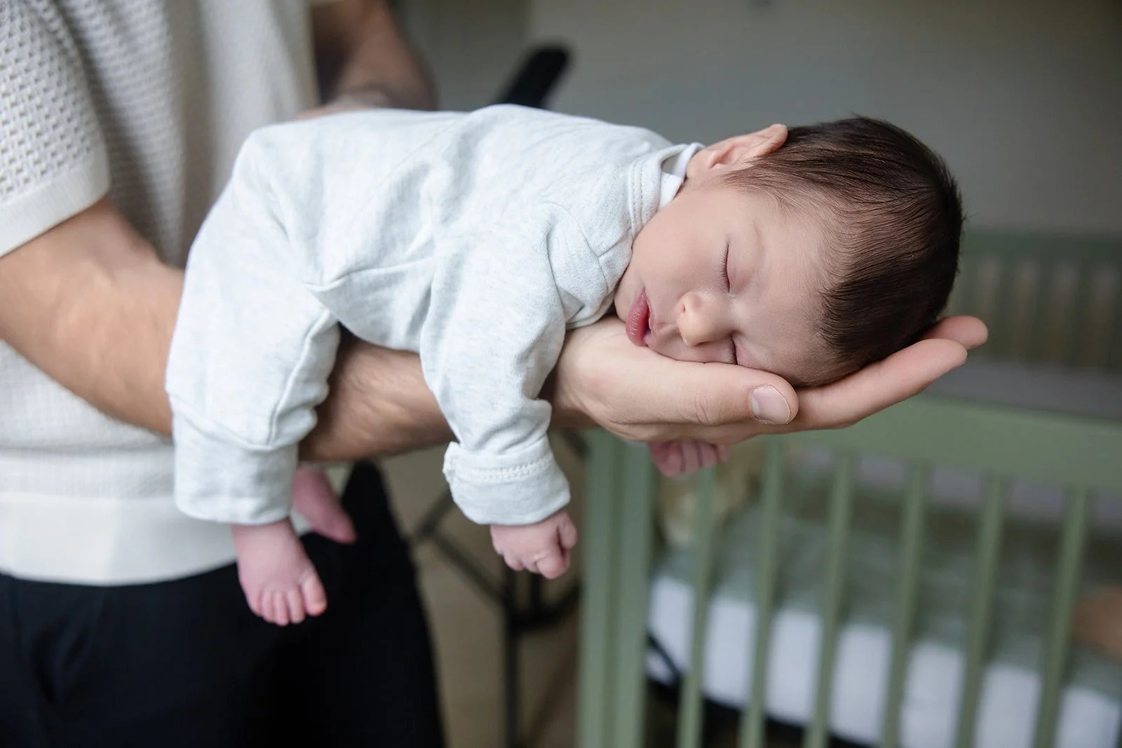A newborn baby with dark hair peacefully sleeping, resting on an adult's hand.