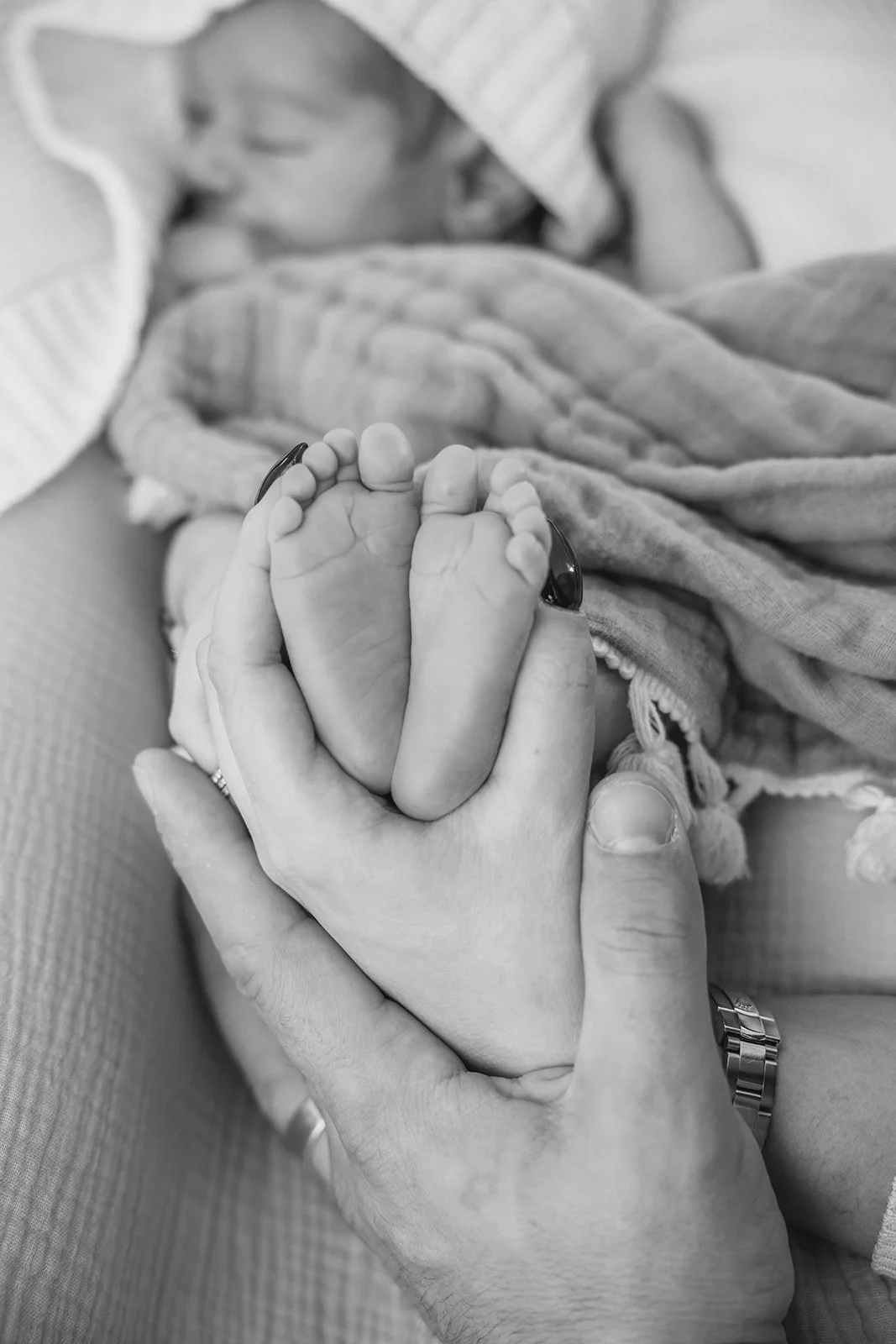 A newborn baby holding an adult's finger with both hands.