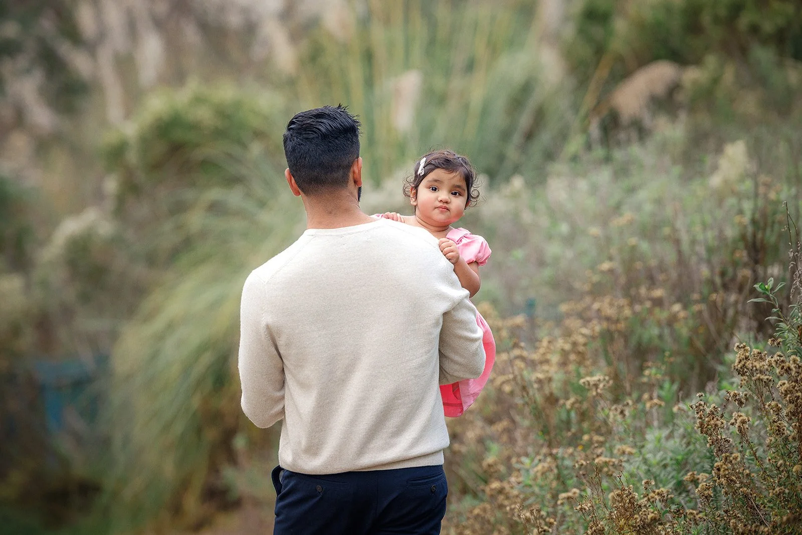 A man holding a young girl in a pink dress in a forested area.