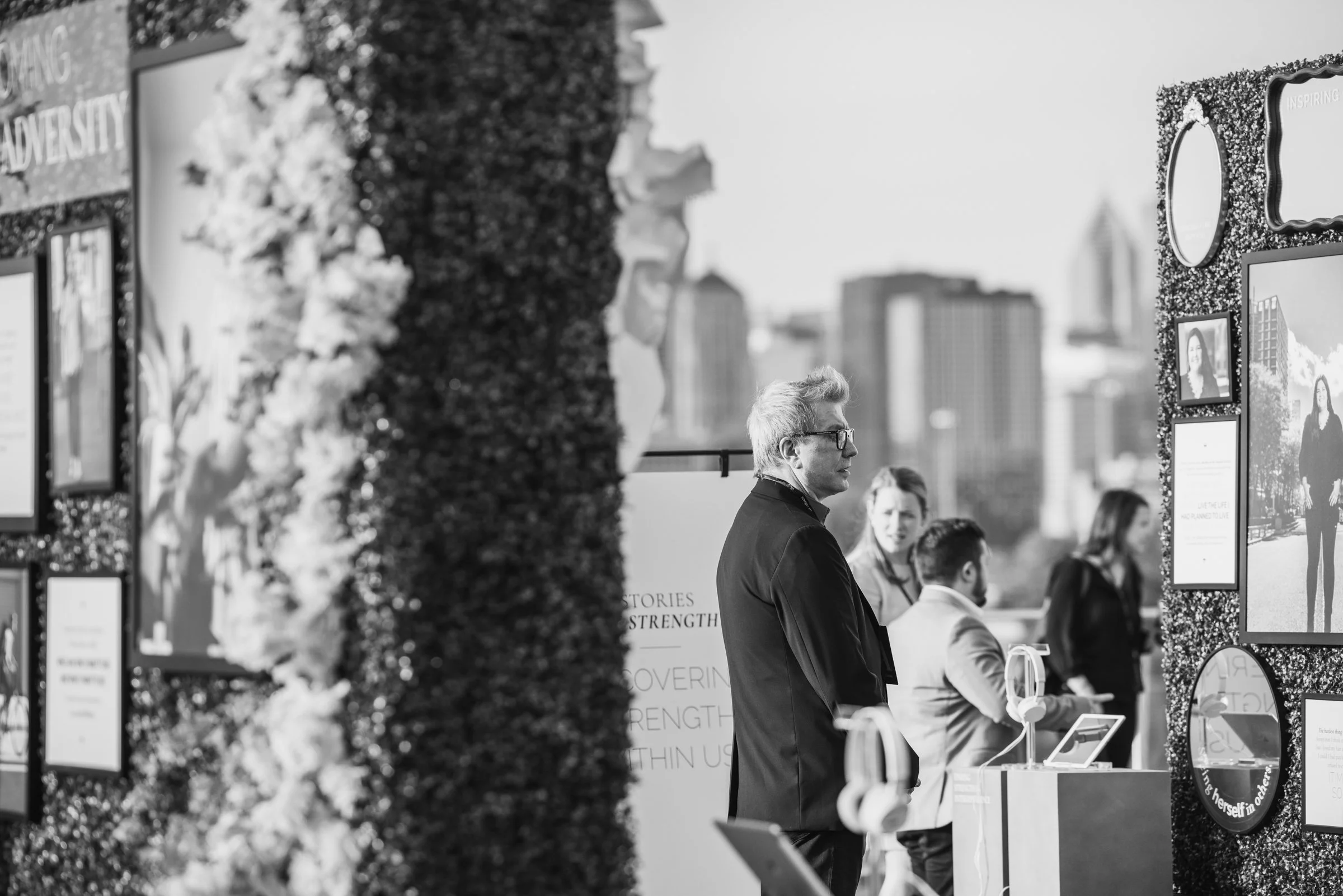 People attending an outdoor exhibition or event with informational displays and screens in front of a cityscape.
