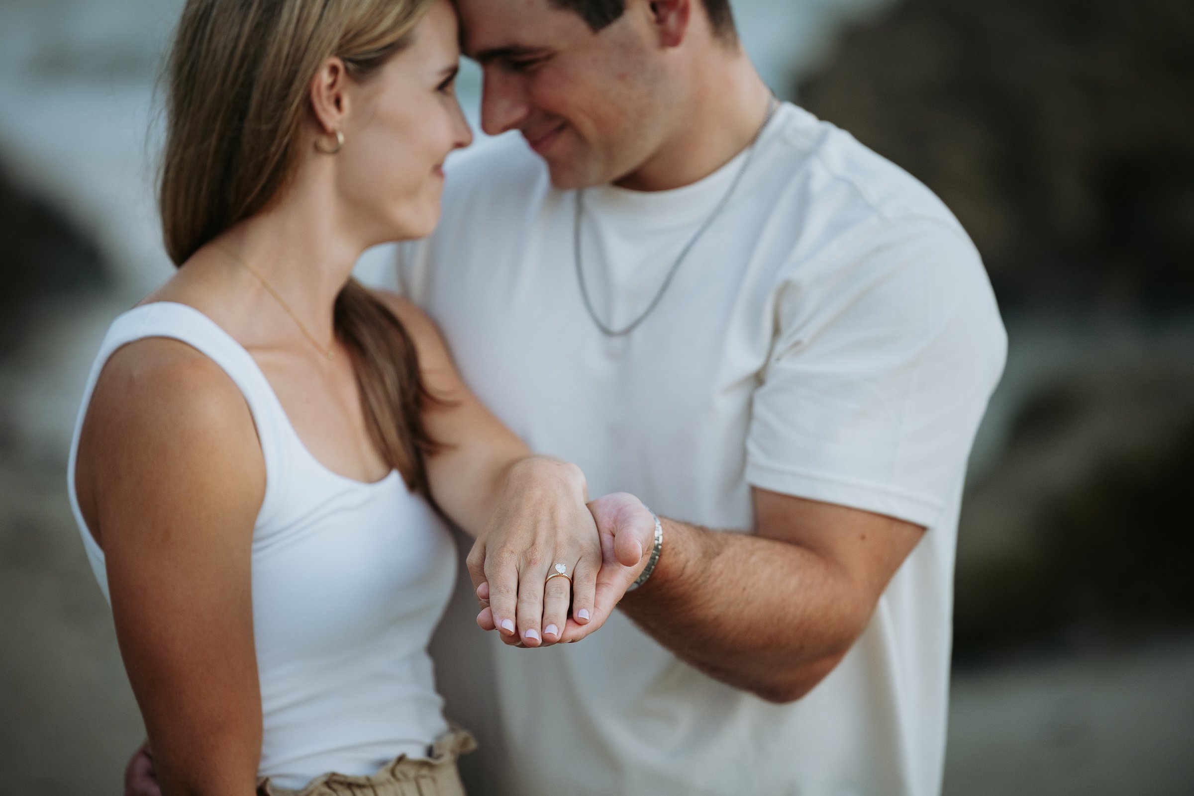 A couple is holding hands with an engagement ring visible, sharing an intimate moment outdoors.