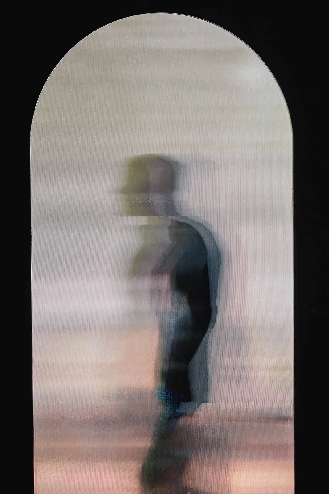 Blurry image of a person standing in front of a light background seen through an arched window or mirror.