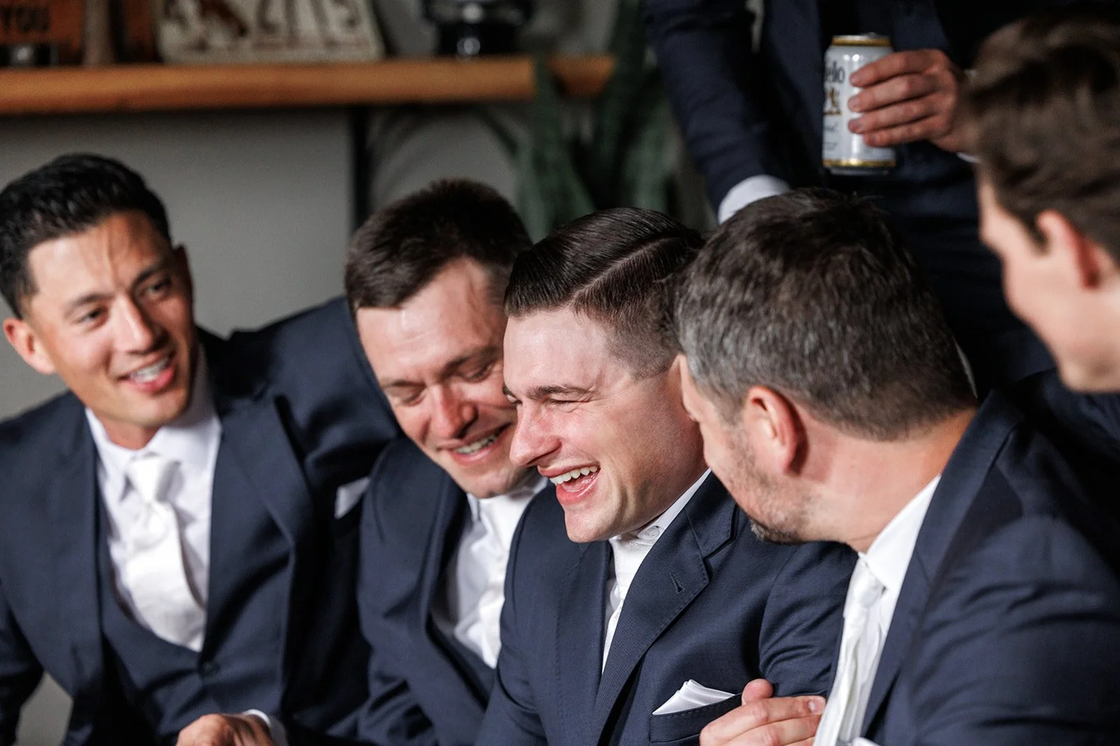 Group of men in suits sitting together, smiling, and laughing at a social gathering.