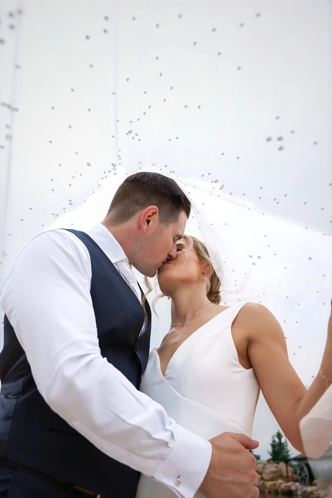 A bride and groom kiss under a transparent umbrella on their wedding day.