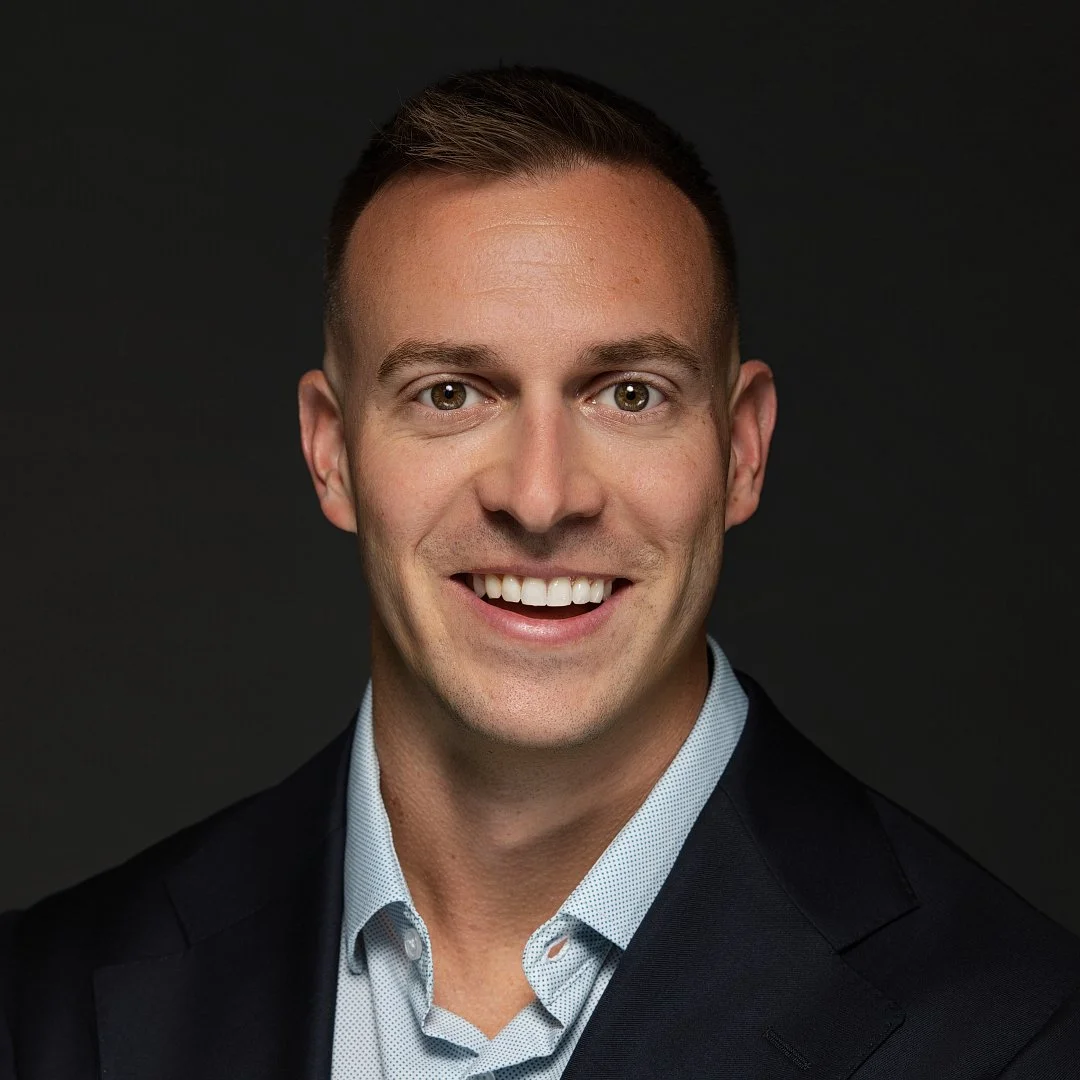 Headshot of a smiling man in a business suit against a dark background.
