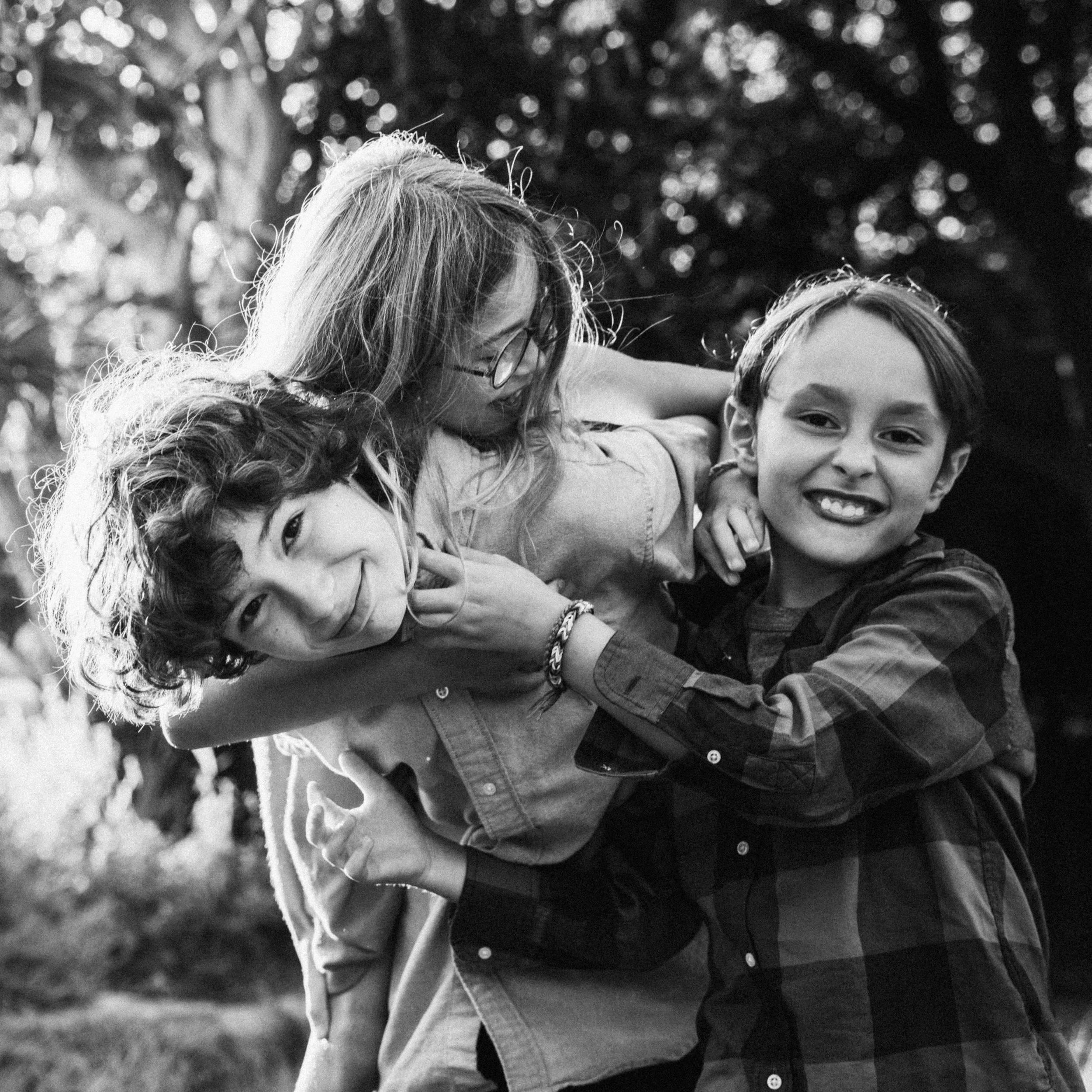 Three children smiling and playing together outdoors in black and white