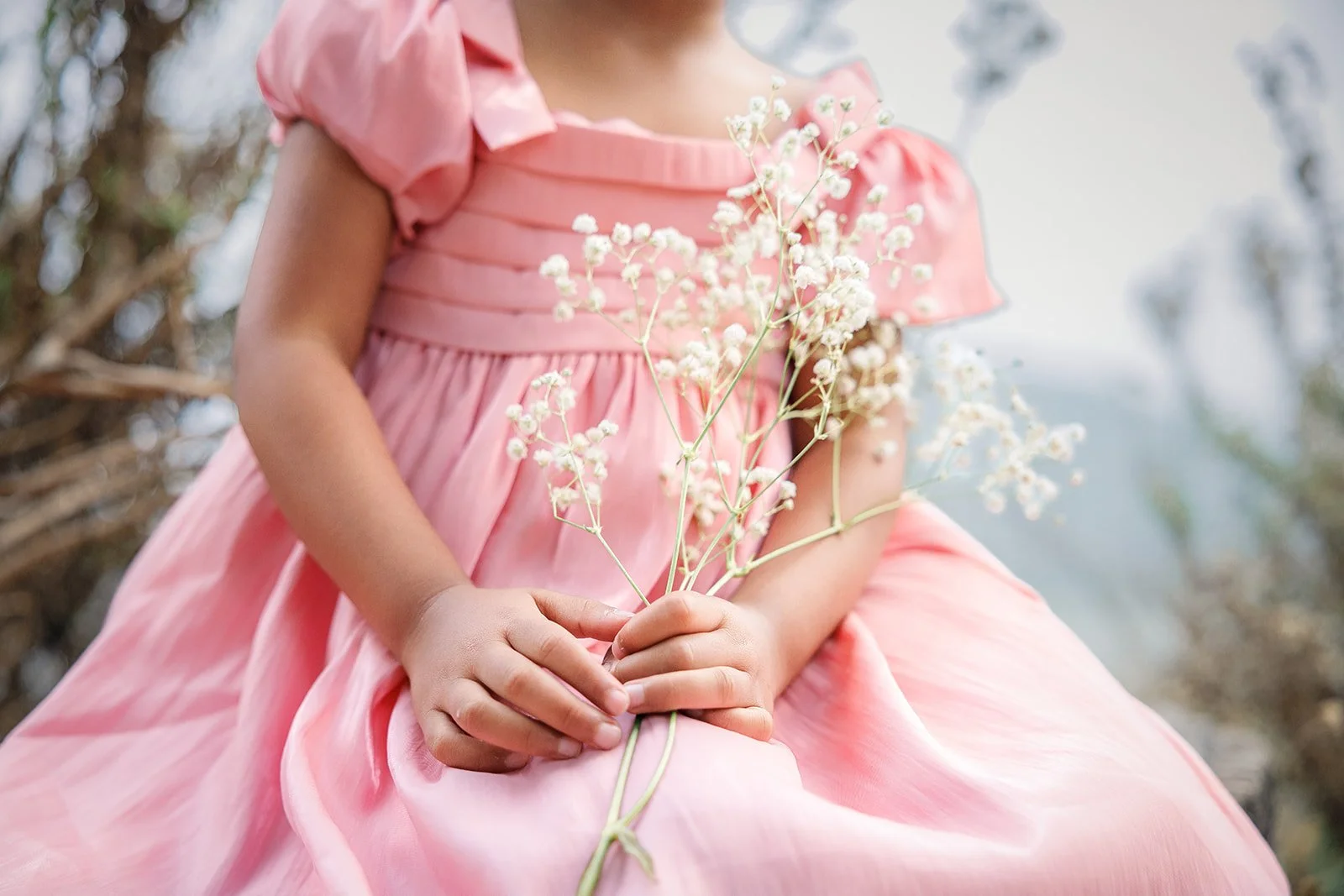 A girl in a pink dress holding a small bouquet of white flowers outdoors.