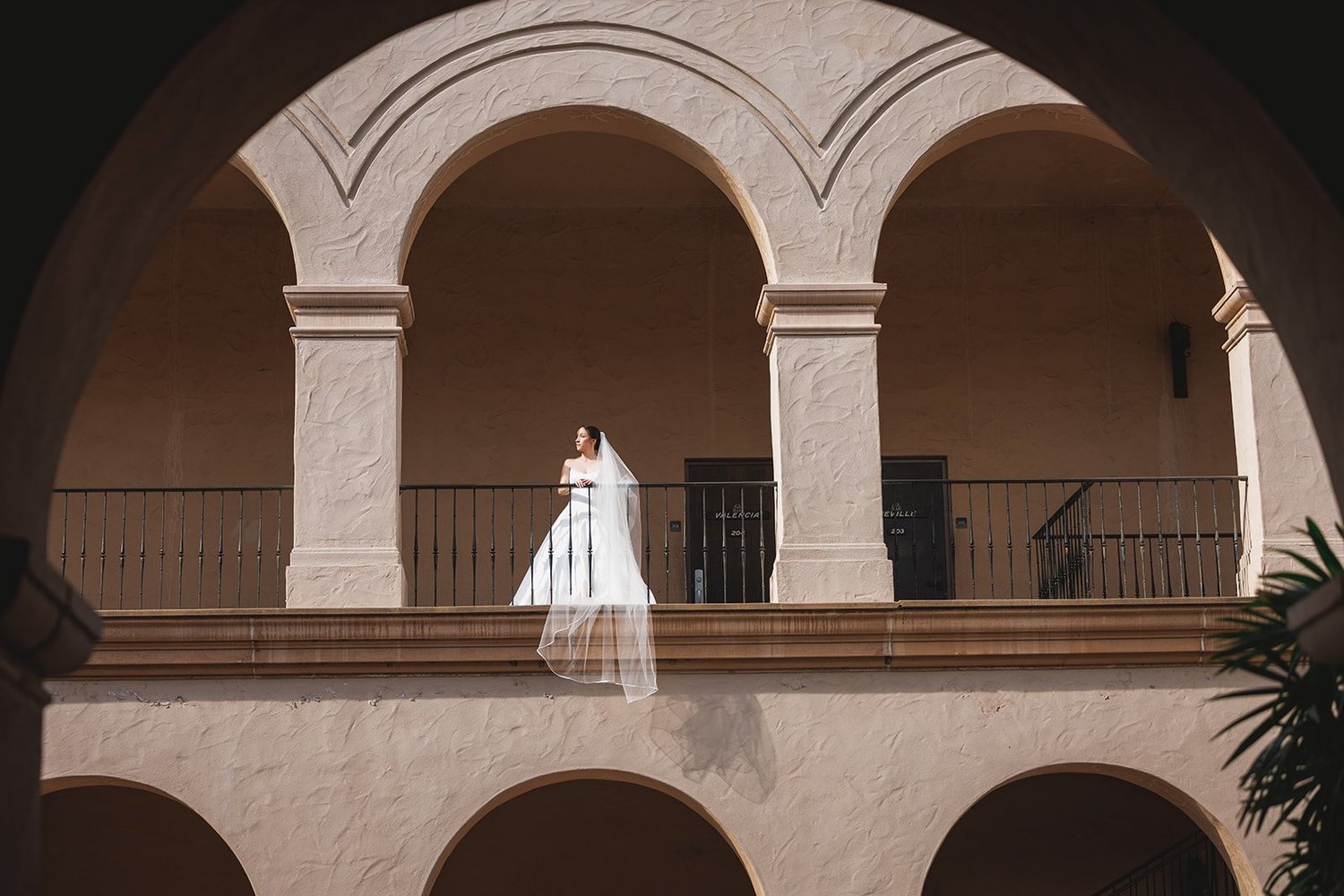 Bride on a balcony framed by Spanish arches in Balboa Park